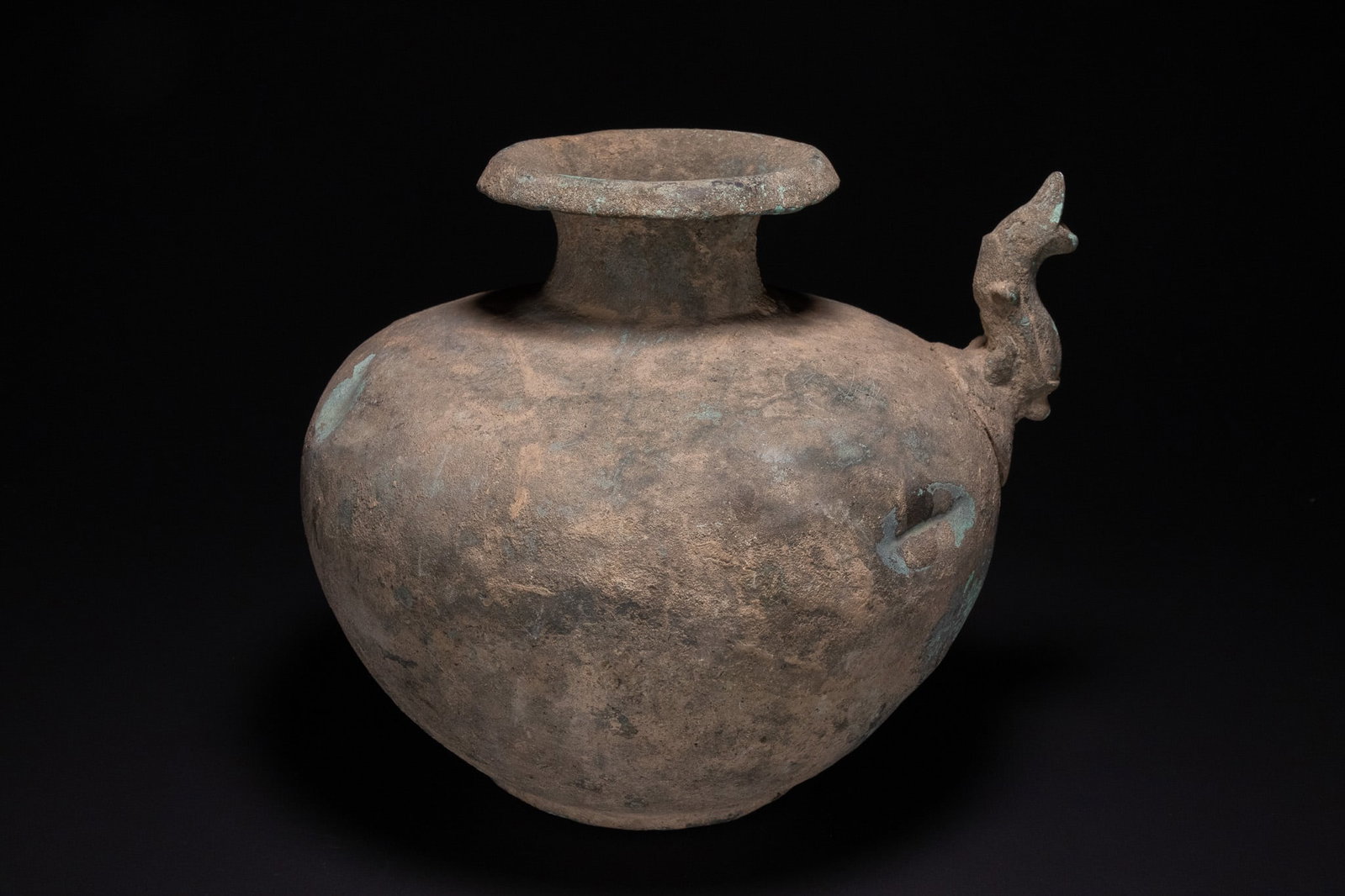 AN INDIAN ZOOMORPHIC BRONZE KENDI, 13TH CENTURY.: A cast copper alloy zoomorphic kendi, or water vessel, of globular form. The vessel features a flared rim above a short neck and a rounded body tapering to a flat base. A prominent spout is cast in th