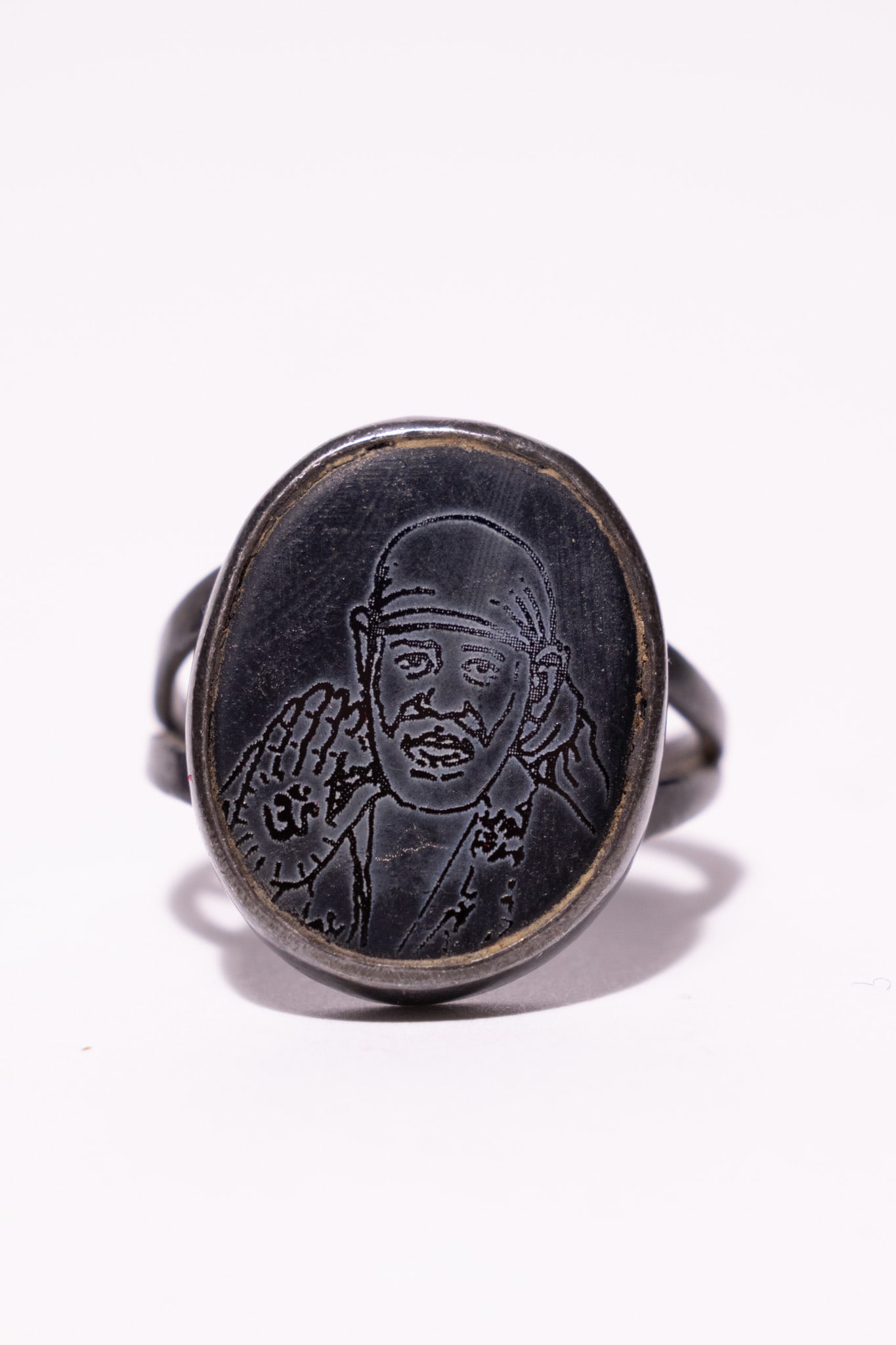 A DEVOTIONAL SILVER SIGNET RING DEPICTING SAI BABA OF SHIRDI.: A devotional signet-style ring featuring an oval black plaque with an intaglio-etched portrait of the Indian spiritual leader, Sai Baba of Shirdi. The figure is depicted in a traditional pose with the