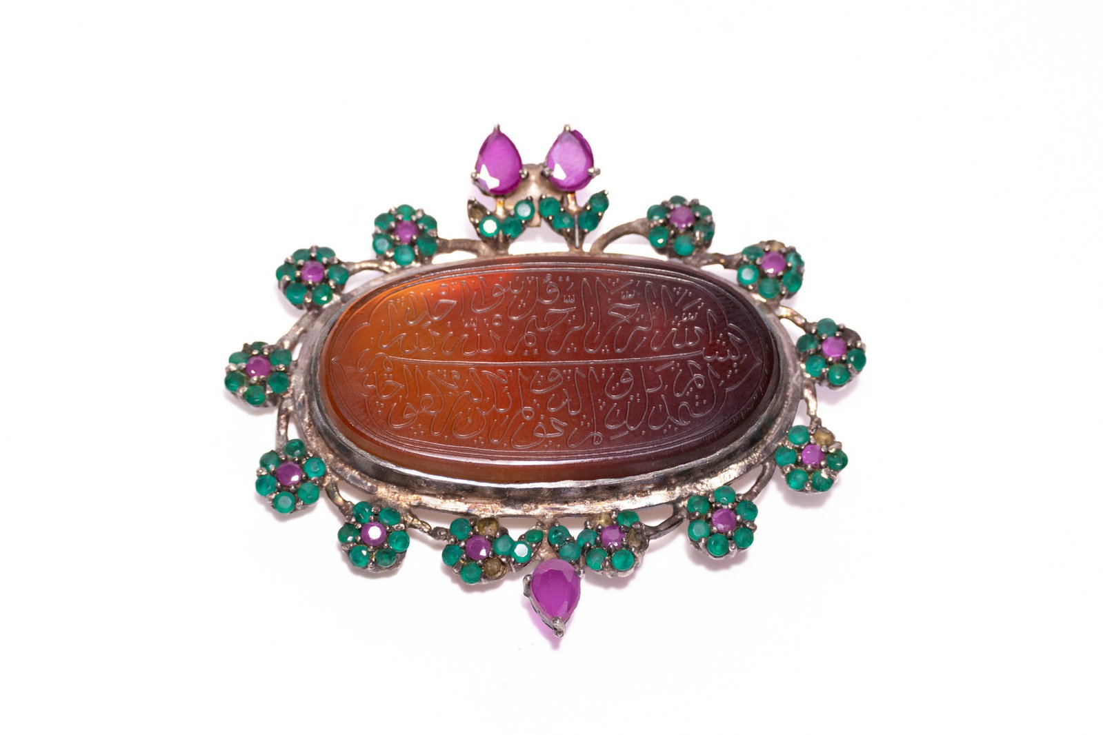 A MUGHAL STYLE GEM-SET SILVER-MOUNTED CARNELIAN TALISMANIC PENDANT.: An Indo-Persian silver-mounted talismanic pendant featuring a large oval central carnelian intaglio. The central stone is finely carved with Arabic calligraphy in Naskh or Thuluth script, arranged in 