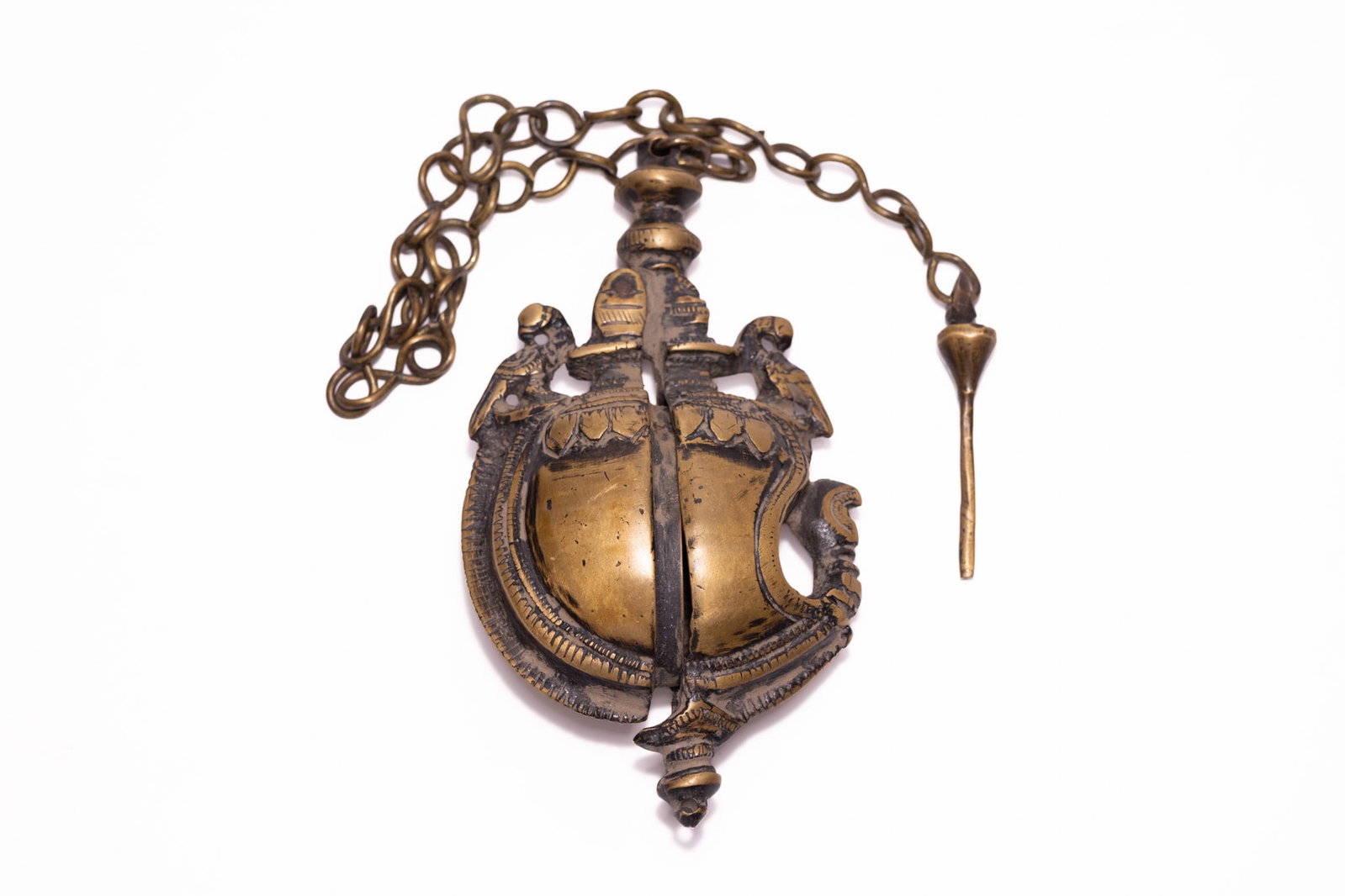 AN INDIAN CAST BRASS SURMEDANI KOHL CONTAINER WITH CHAIN AND APPLICATOR, 19TH CENTURY.: An Indian cast brass surmedani, traditionally used for storing kohl, surma, or vermillion. The object features a bivalve construction with two hinged halves that open vertically. The bulbous, almond-s