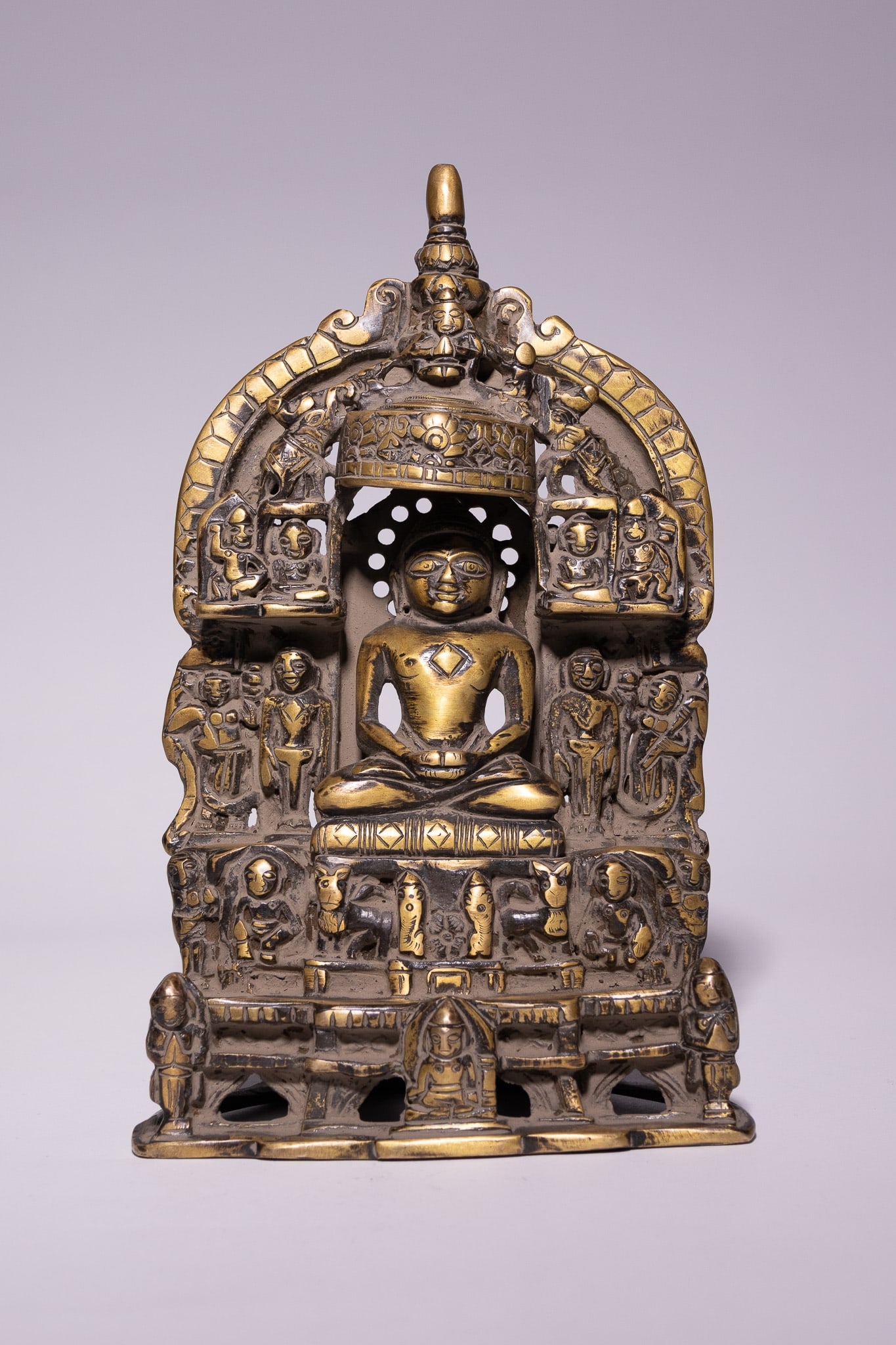 AN INDIAN JAIN BRONZE SHRINE WITH SEATED TIRTHANKARA, 19TH CENTURY.: The bronze cast as a portable Jain shrine centred with a seated Tirthankara figure in meditative posture upon a raised throne, hands resting in dhyana mudra. The figure is framed within an elaborate a
