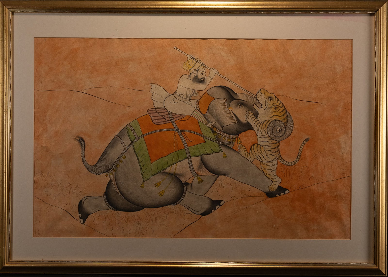 A LARGE INDIAN PAINTING OF A MAHOUT BATTLING A TIGER UPON AN ELEPHANT, 19TH-20TH CENTURY.: The composition depicts a dynamic scene of a mahout seated upon an elephant engaged in combat with a tiger. The elephant strides forward across a gently sloping ground, its body rendered in soft grey 