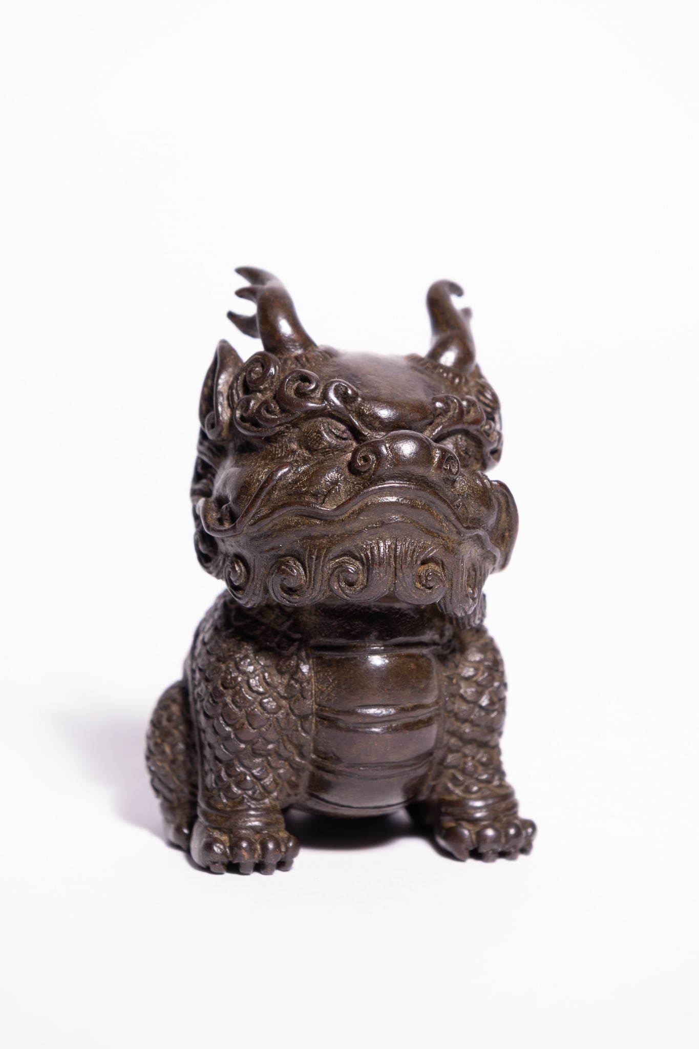 A CHINESE BRONZE FIGURE OF A MYTHICAL BEAST, XUANDE MARK.: A cast bronze figure of a mythical beast, possibly a qilin or bixie, depicted in a seated, squat posture. The creature is characterised by a broad snout with flared nostrils, bulging eyes, and a styli