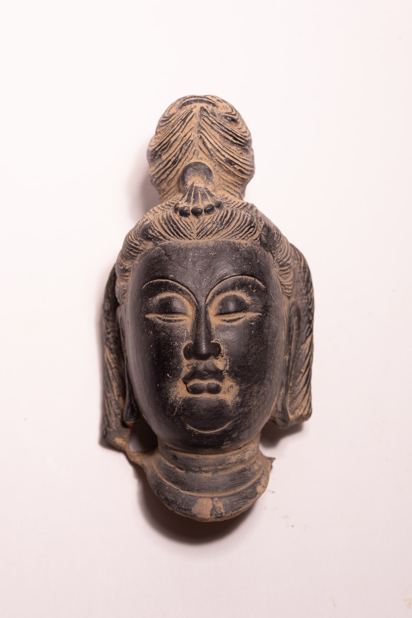 A CHINESE BLACK-FIRED CERAMIC HEAD FRAGMENT OF A BODHISATTVA.: A Chinese ceramic sculpture fragment depicting the head of a Bodhisattva or female deity. The piece is constructed from dark grey to black-fired earthenware or stoneware with a hollow interior. The fa