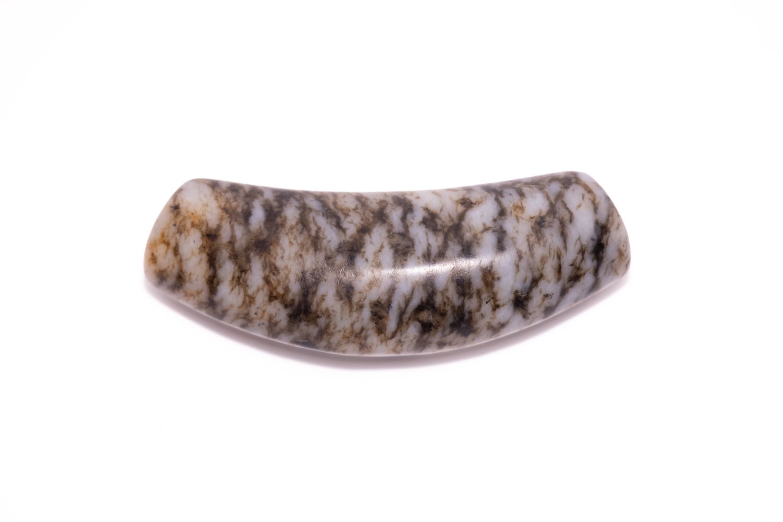 A CHINESE CARVED MOTTLED JADE ARCUATE BEAD.: A carved and polished tubular bead of arcuate form, fashioned from a mottled jade. The stone displays a complex natural pattern of dendritic or moss-like inclusions in shades of dark brown, charcoal, 