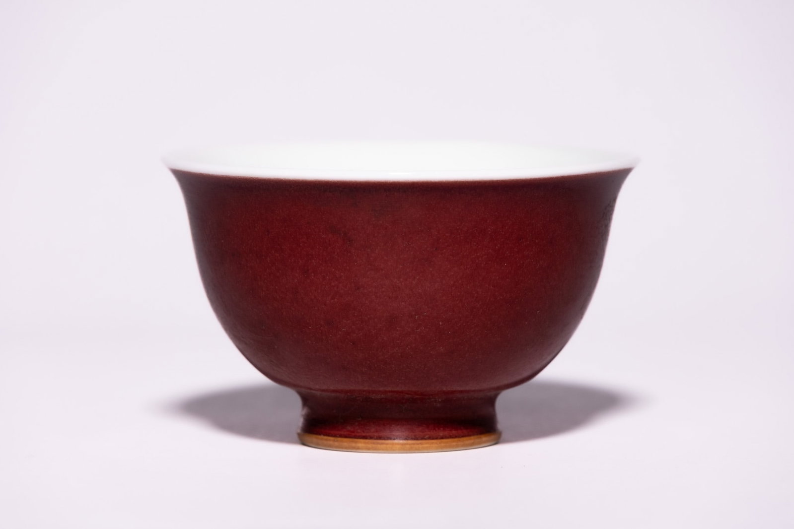 A CHINESE OXBLOOD-GLAZED BOWL WITH FLARED RIM AND FOOTED BASE.: The bowl of elegant, gently flared form rising from a short, neatly defined foot to a wide rim, the exterior covered in a rich, deep red glaze with subtle tonal variations and soft mottling throughout