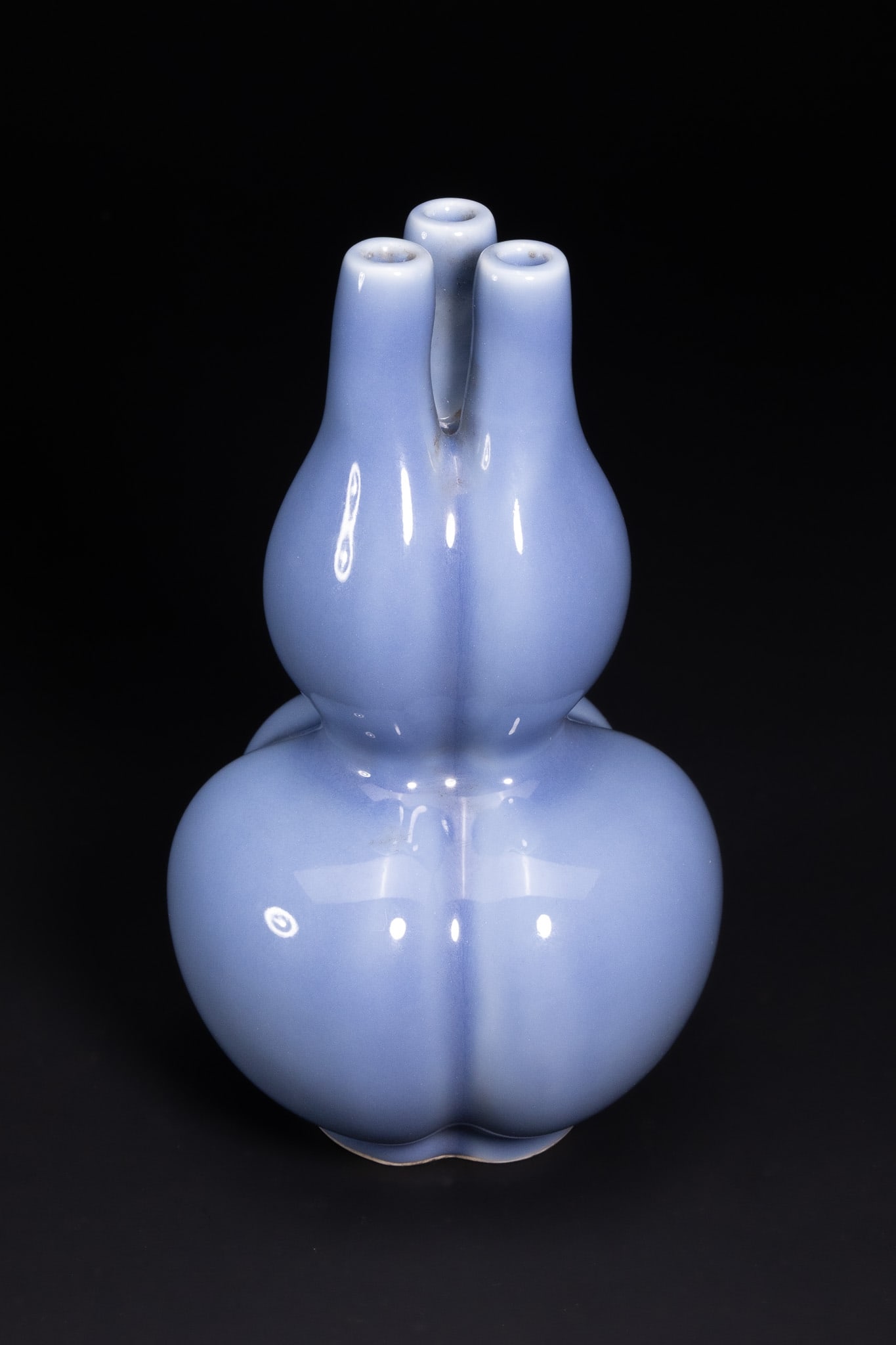 A CHINESE CLAIR-DE-LUNE GLAZED TRIPLE-GOURD VASE, QIANLONG MARK.: A Chinese porcelain vase of double-gourd form, rising to three slender tubular necks emerging from the upper section. The body is covered in a soft, even pale blue clair-de-lune glaze with a smooth, g