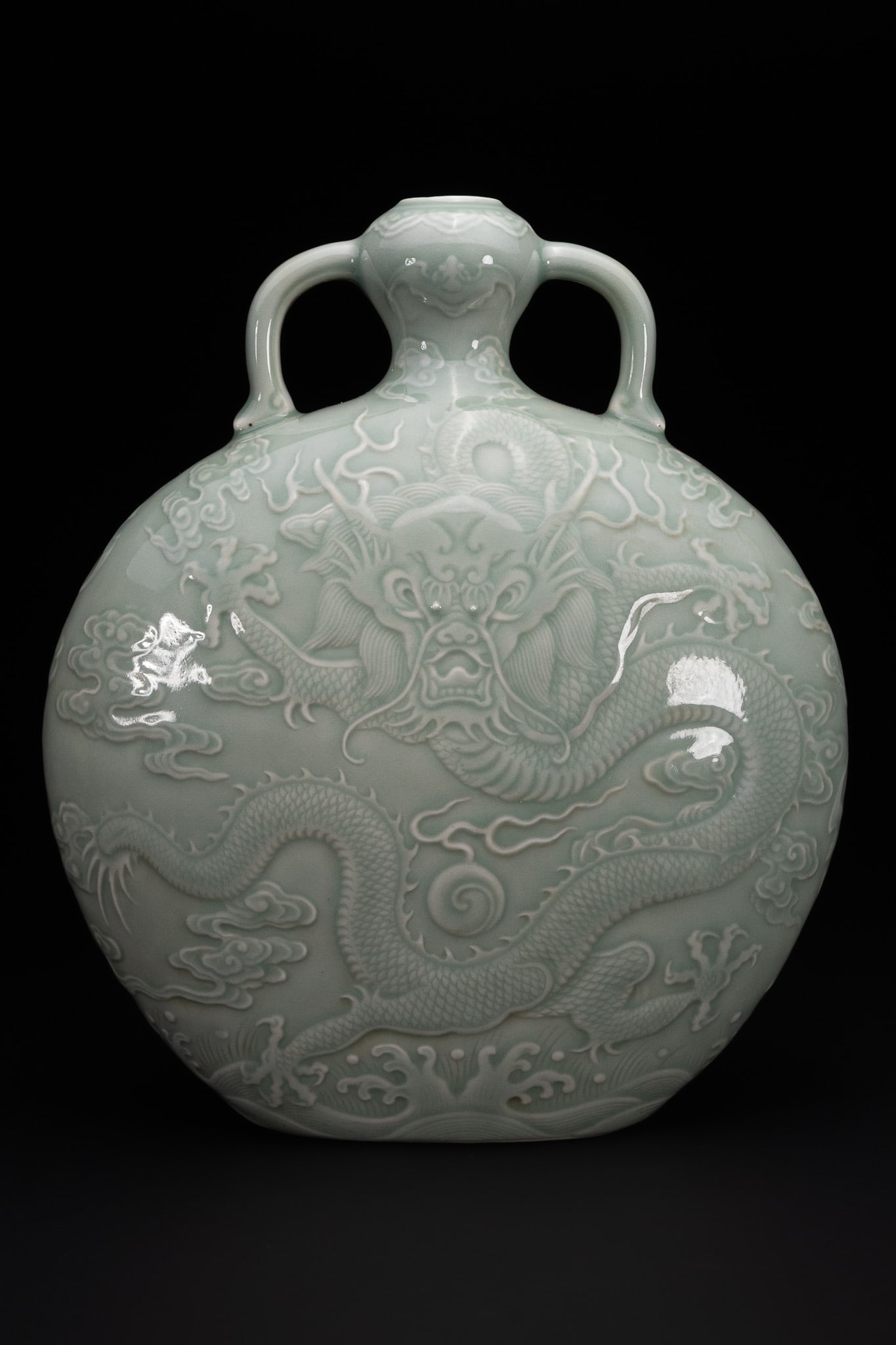 A CHINESE CELADON-GLAZED 'DRAGON' MOON FLASK, QIANLONG MARK.: A finely potted porcelain moon flask of flattened circular form, rising to a short neck and flanked by a pair of loop handles extending from the shoulder to the neck. The body is covered in a soft cel