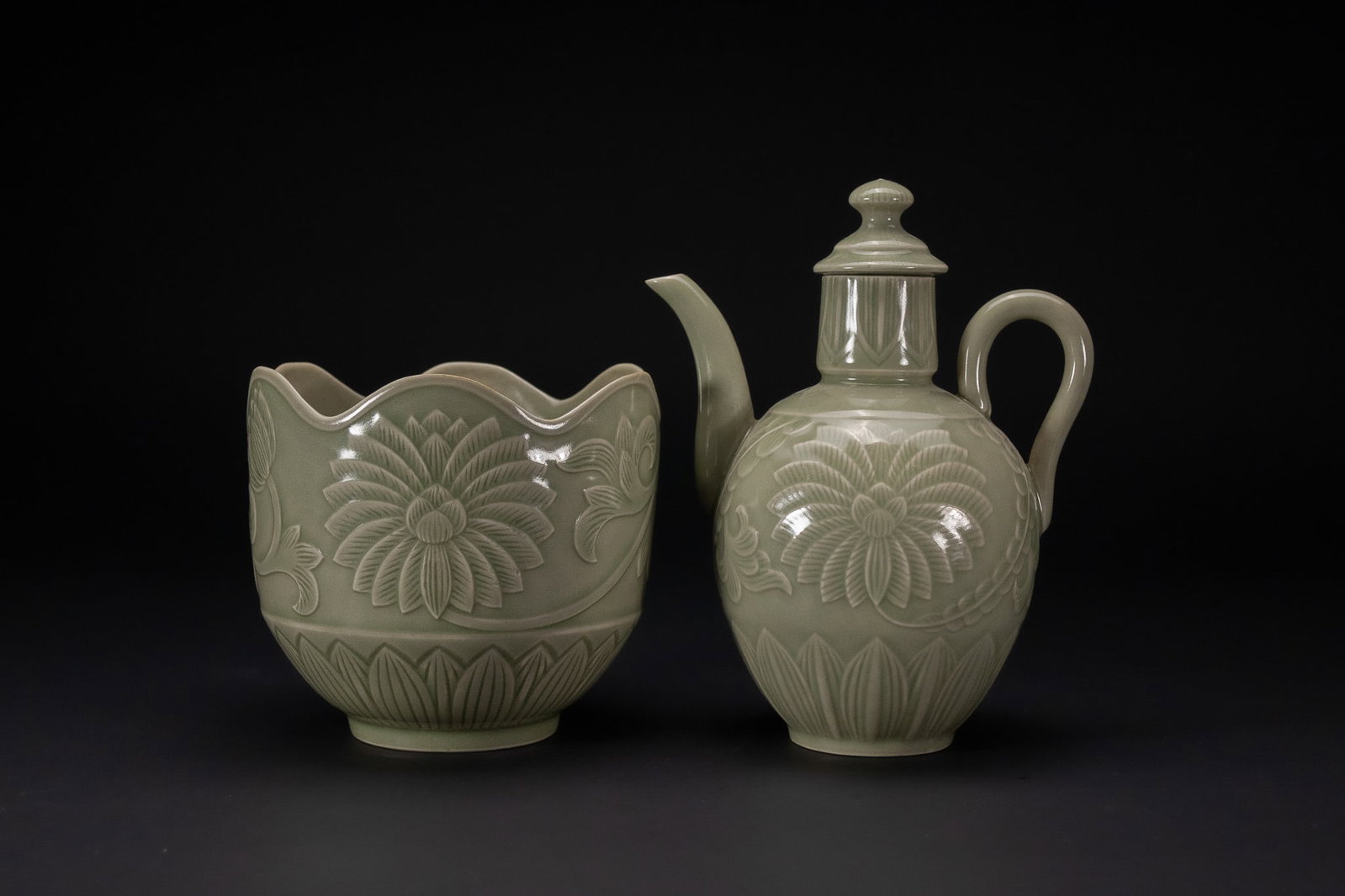 A CHINESE CELADON-GLAZED EWER AND WARMING BOWL.: A Chinese celadon-glazed stoneware ewer and matching warming bowl set. The ewer is designed with an ovoid body, a curved spout, and a loop handle, featuring a tiered lid with a bud-shaped finial. The 