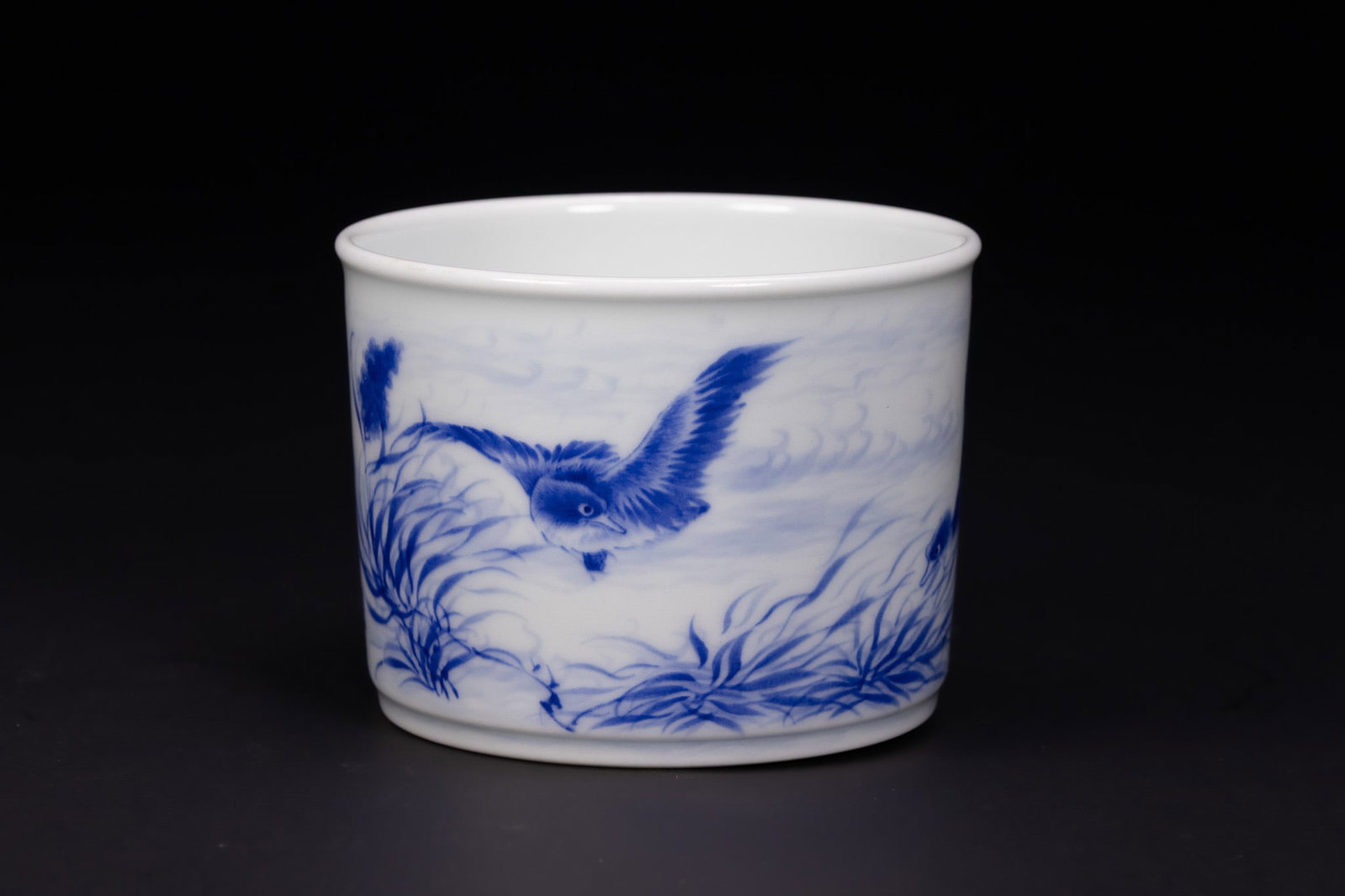 A CHINESE BLUE AND WHITE PORCELAIN WASHER, WANG BU MARK.: A cylindrical porcelain brush pot of bitong form with a flat, recessed base. The exterior is decorated in underglaze cobalt blue with a continuous landscape scene depicting birds in flight amongst swa