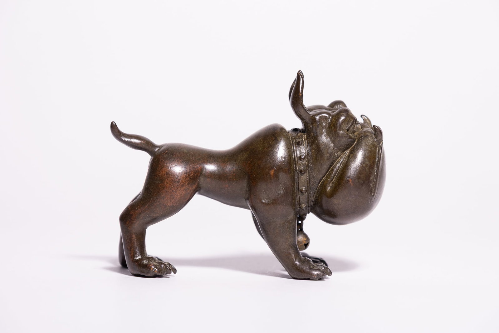 A JAPANESE CAST BRONZE FIGURINE OF A BULLDOG.: A cast bronze figurine of a bulldog, rendered in an alert standing posture and designed in a stylised, caricatured manner. The dog features a disproportionately large, rounded muzzle with prominent, w