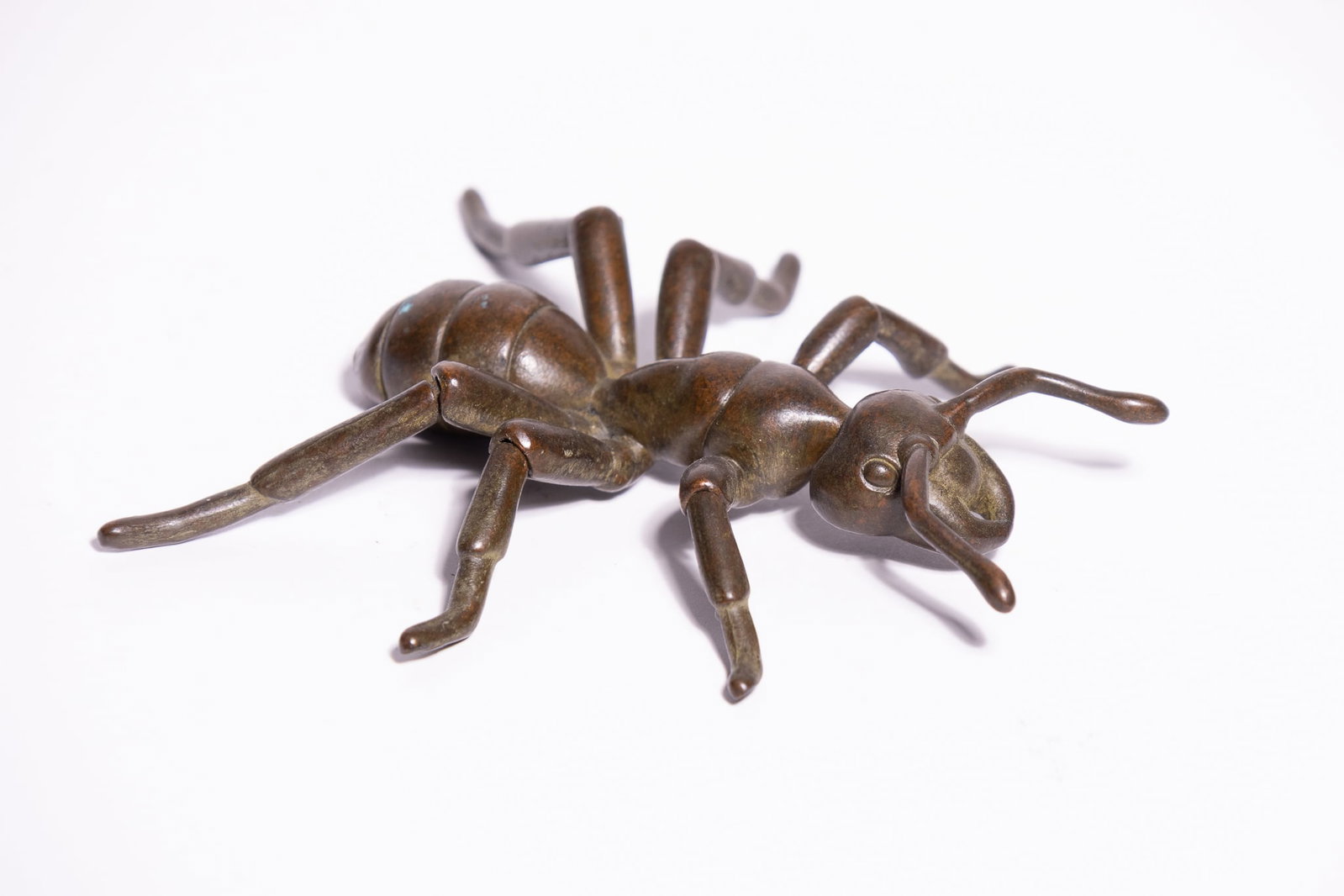 A JAPANESE BRONZE ARTICULATED MODEL OF AN ANT.: A cast bronze model of an ant, rendered with a three-part segmented body and six jointed legs. The figure is detailed with protruding eyes and a pair of curved antennae. The bronze surface is finished