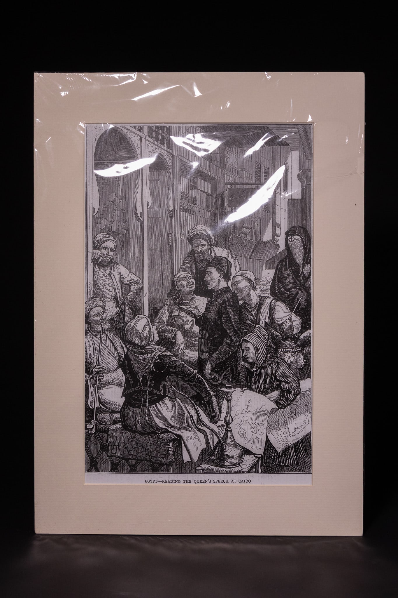 READING THE QUEEN'S SPEECH AT CAIRO, PRINT, LATE 19TH CENTURY.: Titled Egypt - Reading the Queen's Speech at Cairo, the print depicts a crowded Cairo street scene with various figures in traditional Egyptian attire, including turbans and veils, listening to a man 
