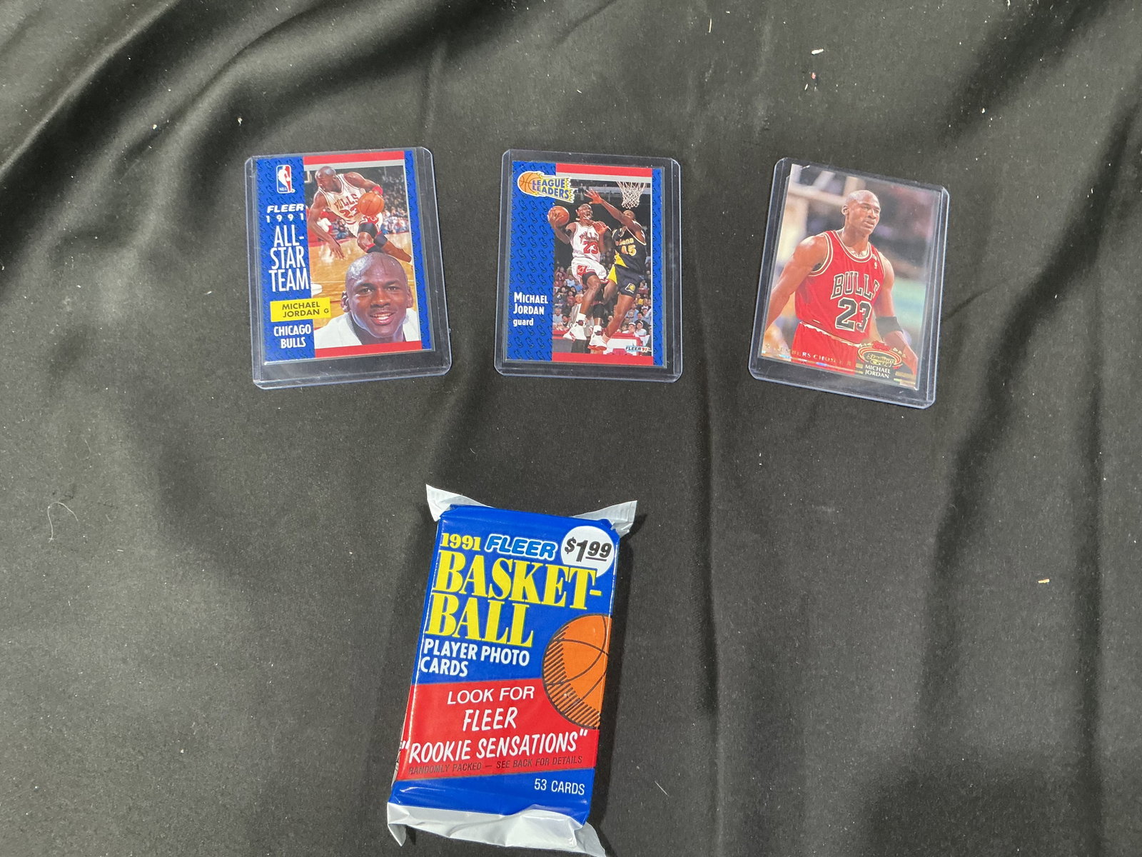Michael Jordan Basketball Cards Lot with 1991 Fleer Pack: Lot of three Michael Jordan trading cards including a Fleer All-Star Team card, a Fleer League Leaders action card, and a premium Bulls portrait card. All cards sleeved for protection. Includes one se