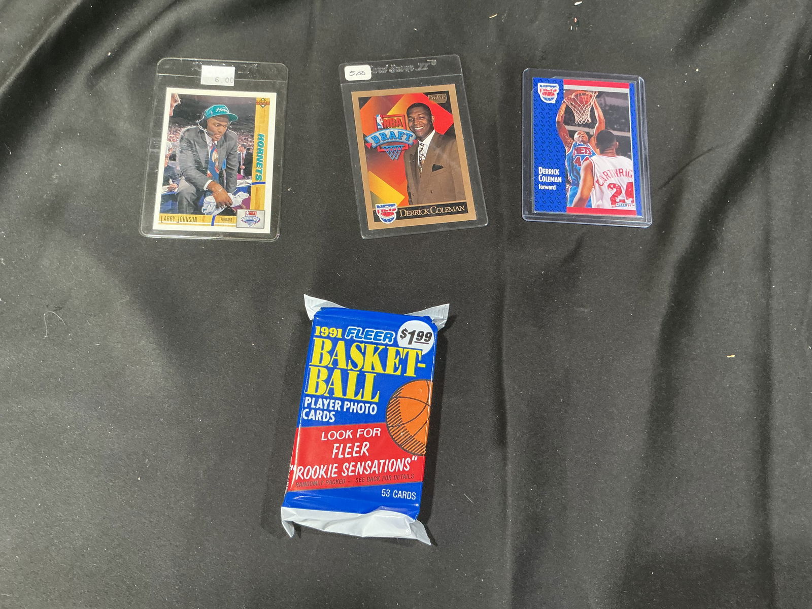Basketball Cards Lot: Larry Johnson, Derrick Coleman & Draft Card + 1991 Fleer Pack: Lot of three vintage basketball trading cards including a Larry Johnson Hornets card, a Derrick Coleman NBA Draft card, and a Derrick Coleman action card. All cards are sleeved. Includes one sealed 19