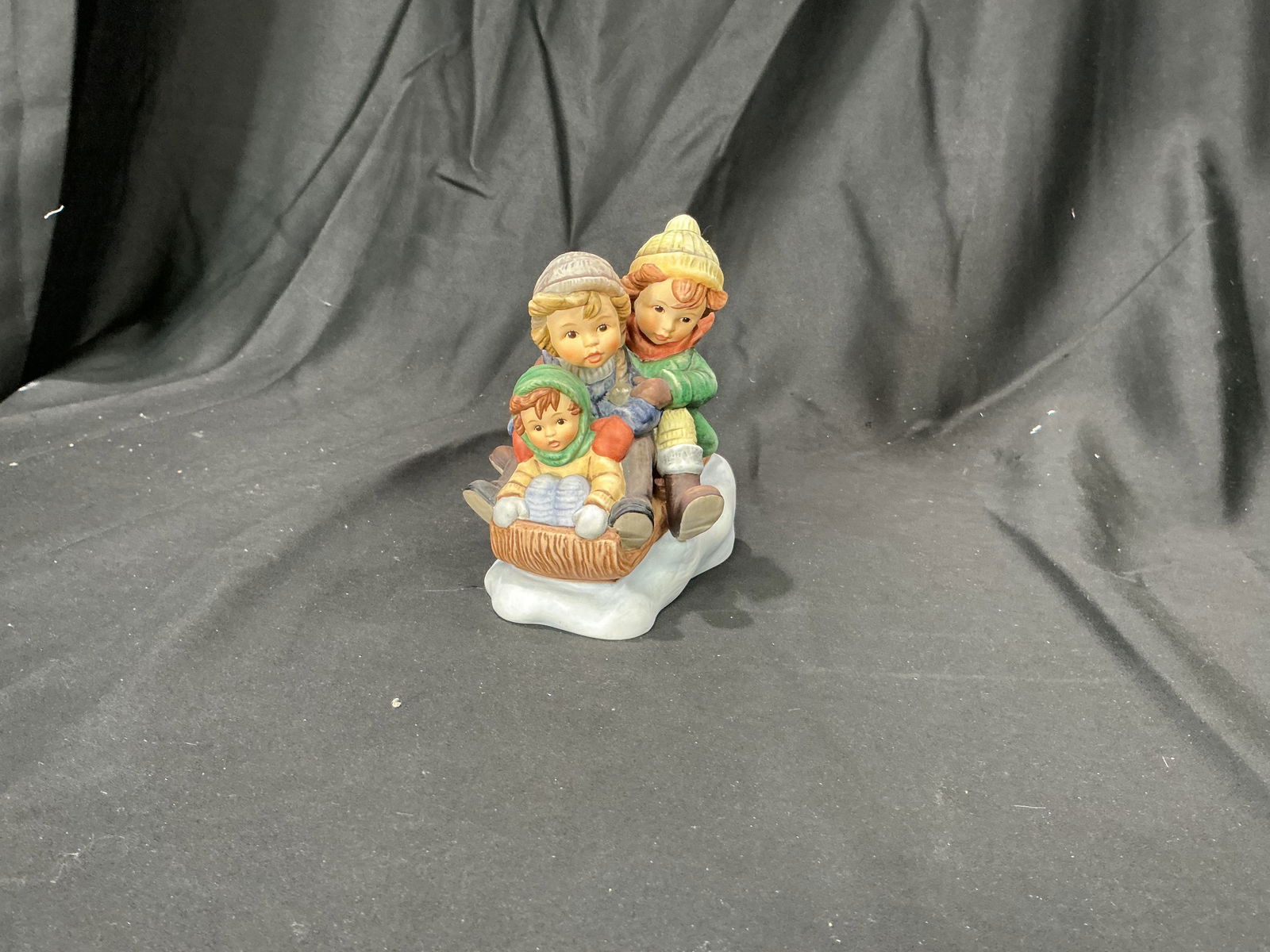 2004 Goebel Hummel Downhill Dash BH 1238 Figurine: Charming Goebel Hummel figurine titled Downhill Dash (BH 1238), dated 2004. Features three bundled-up children racing downhill on a sled, beautifully hand-painted in the classic Berta Hummel tradition