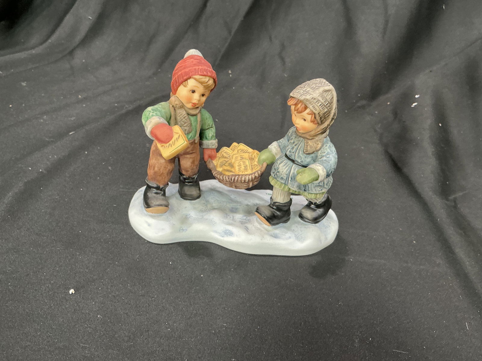 2003 Goebel Hummel Season's Greetings BH 254 Figurine: Heartwarming Goebel Hummel figurine titled Season's Greetings (BH 254), dated 2003. Depicts two children bundled for winter, carrying a basket filled with wrapped presents. Finely hand-painted with cl