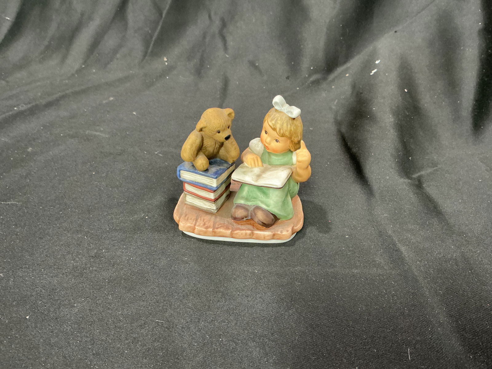 2002 Goebel Hummel A Tall Tale BH 183 Figurine: Adorable Goebel Hummel figurine titled A Tall Tale (BH 183), dated 2002. Features a young girl reading from an open book while her teddy bear listens eagerly from atop a stack of books. A sweet, imagi