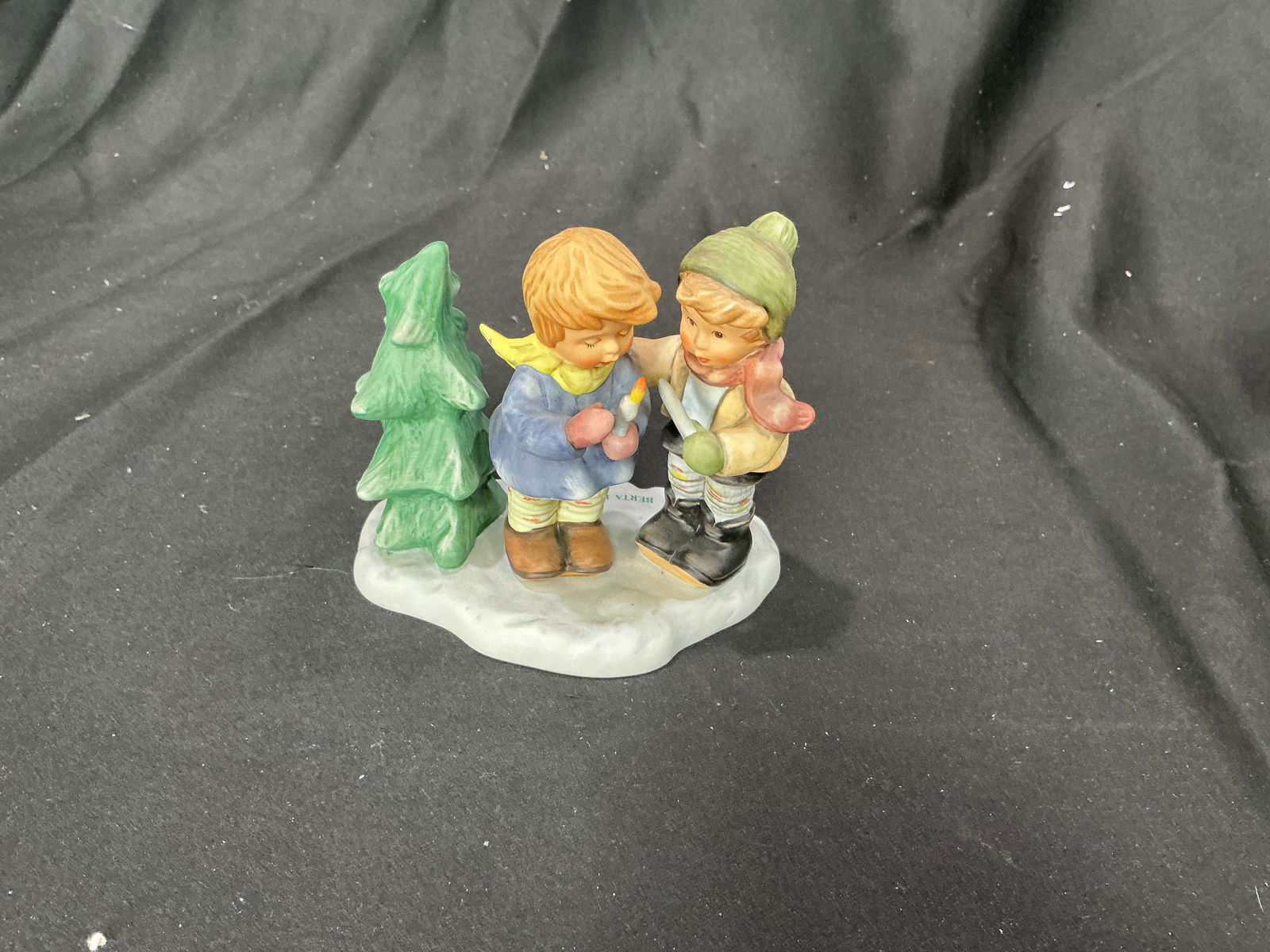 Goebel Berta Hummel Light the Night Figurine (BH 59, 1998): Charming Goebel Berta Hummel figurine titled 'Light the Night' (BH 59), dated 1998. Features two children holding a candle beside a tree. A sweet winter-themed collectible.