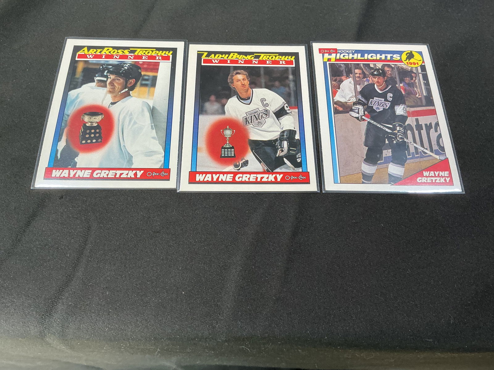 Three Wayne Gretzky hockey cards - trophy winners & highlights: Group of three Wayne Gretzky hockey trading cards, including O-Pee-Chee trophy winner cards (Art Ross Trophy Winner and Lady Byng Trophy Winner) and a Gretzky highlights card. Cards appear to be from