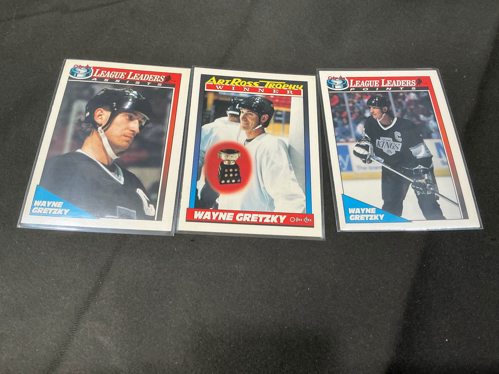 Three Wayne Gretzky hockey cards - league leaders & trophy winner: Lot of three vintage Wayne Gretzky NHL trading cards, featuring league leaders and trophy winner themes. Includes League Leaders (Assists), Art Ross Trophy Winner, and League Leaders (Points) cards,