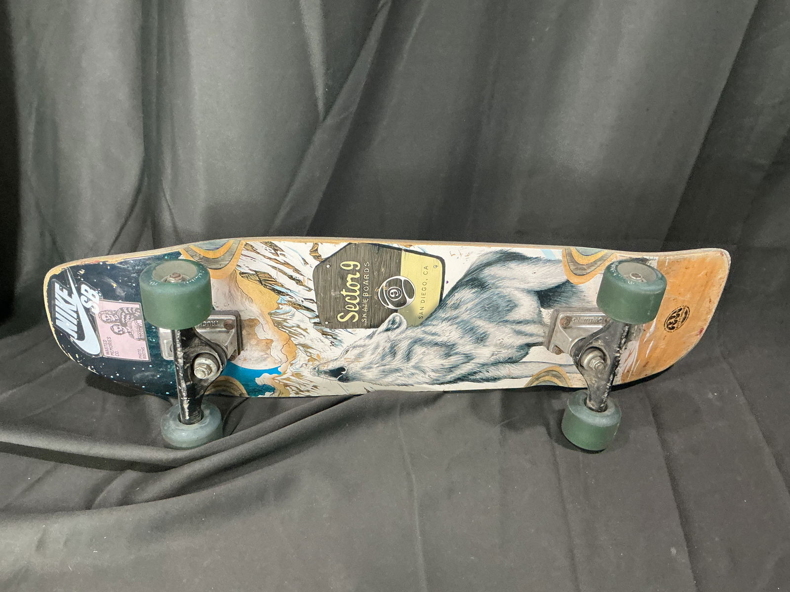 Vintage Sector 9 complete skateboard with wolf graphic: Complete skateboard by Sector 9 featuring a wolf graphic deck with printed branding, fitted with metal trucks and green wheels. The top retains applied grip tape with visible use. This appears to be a