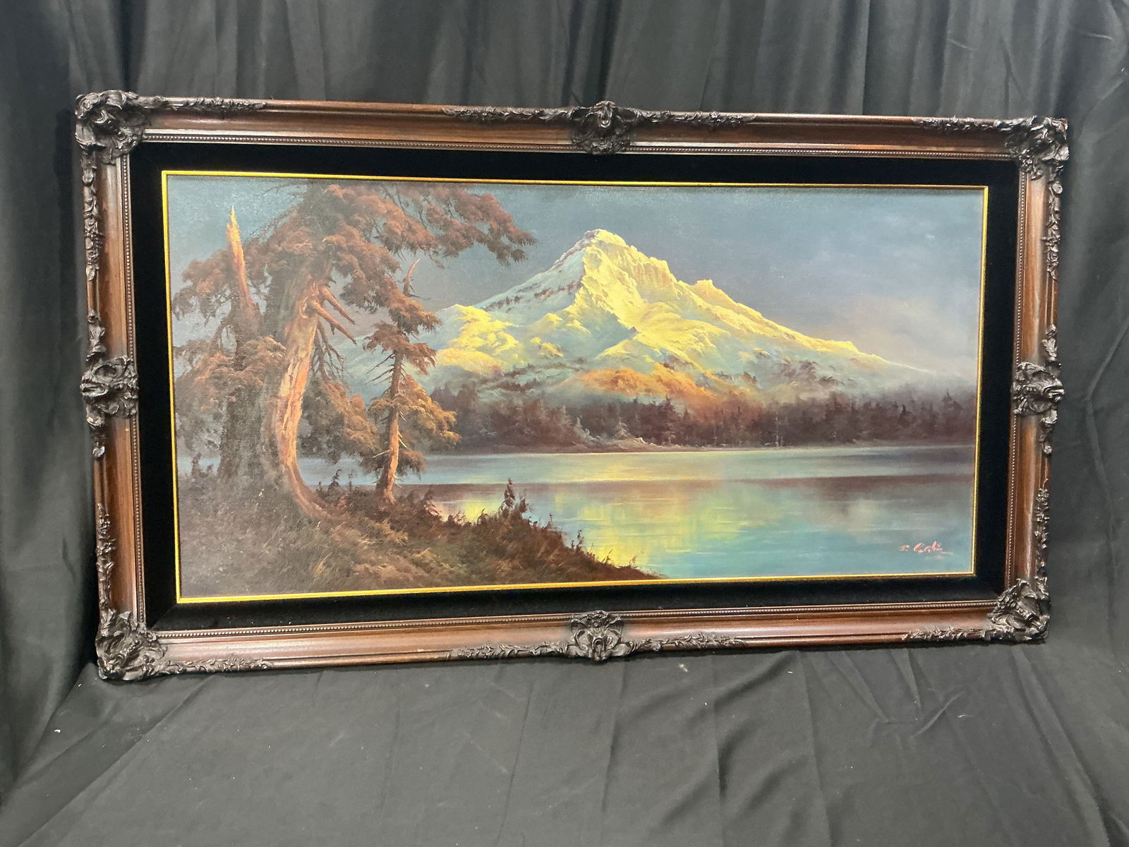 Mountain Landscape Painting by Eugene Garin (1978): Original mountain landscape painting by Eugene Garin depicting a snow-capped peak rising above a tranquil lake, framed by evergreen trees along the shoreline. Warm light illuminates the mountain