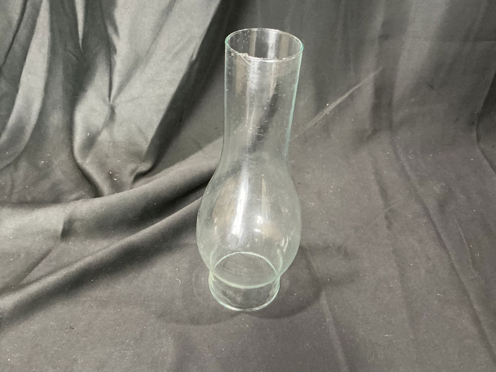Clear glass oil lamp chimney: Clear glass chimney for an oil or kerosene lamp, featuring a flared upper rim and a fitted lower collar for mounting to a burner assembly. Suitable as a replacement chimney or for decorative display.