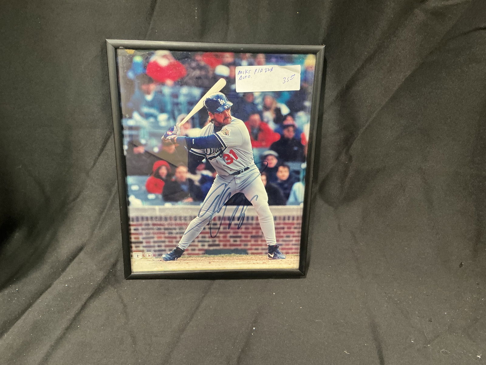 Mike Piazza Autographed 8x10 Photo Los Angeles Dodgers Batting Action Framed: Dynamic 8x10 color photograph of Hall of Famer Mike Piazza in his Los Angeles Dodgers uniform (#31) mid-swing during a game. Boldly hand-signed in blue Sharpie across the lower portion of the image.