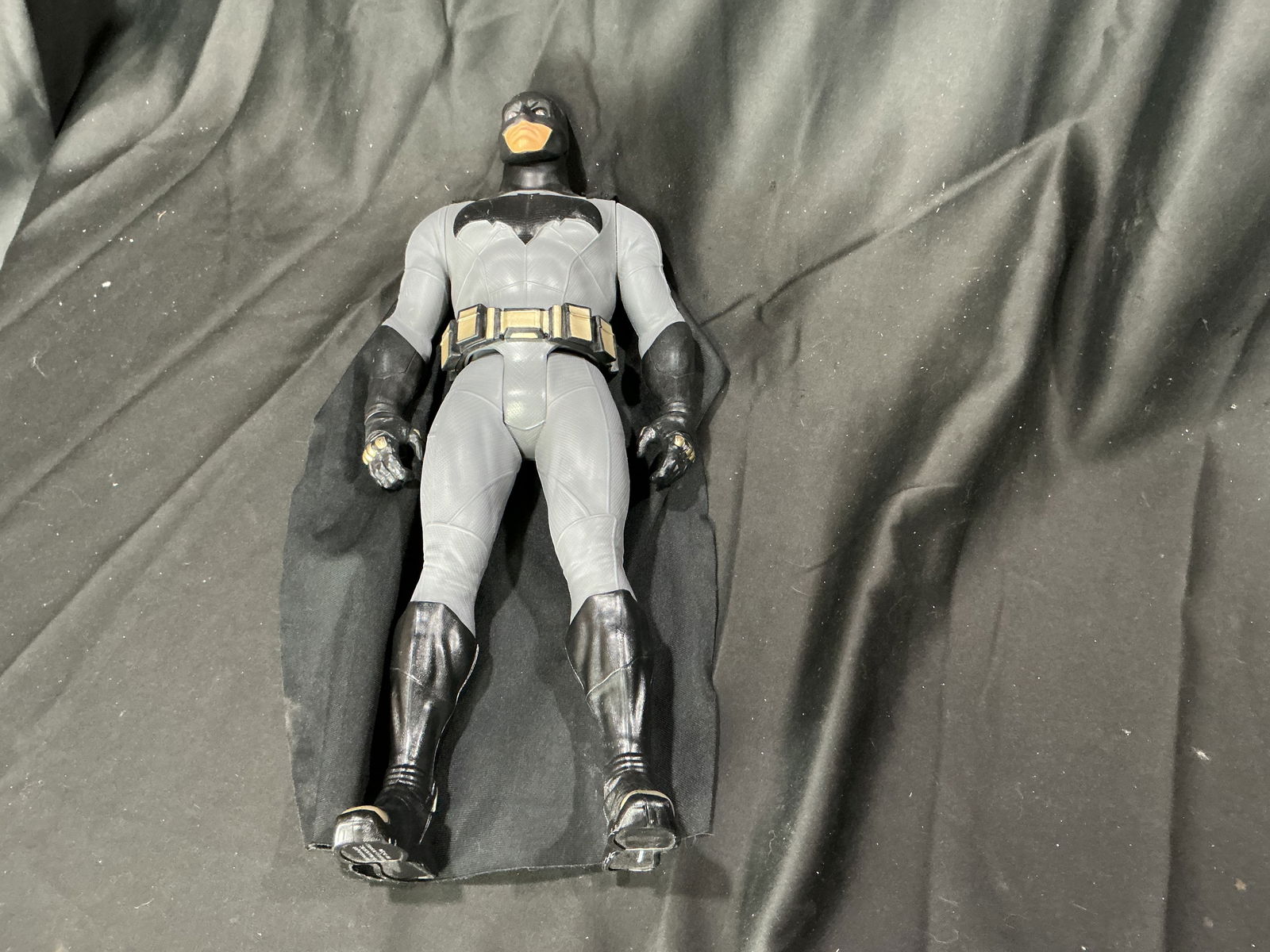 Large Batman Action Figure with Fabric Cape: Large-format Batman action figure depicting the DC Comics superhero in a gray and black suit with black boots, gloves, utility belt, and black fabric cape. The figure features molded costume detailing