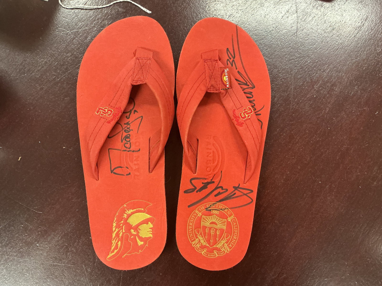 USC Trojans Signed Rainbow Flip Flops Multi Player Autographs including Markus Allen: Pair of University of Southern California Trojans themed Rainbow brand flip flops featuring multiple player signatures. Red with USC logos and several bold autographs including numbers 32 and others.