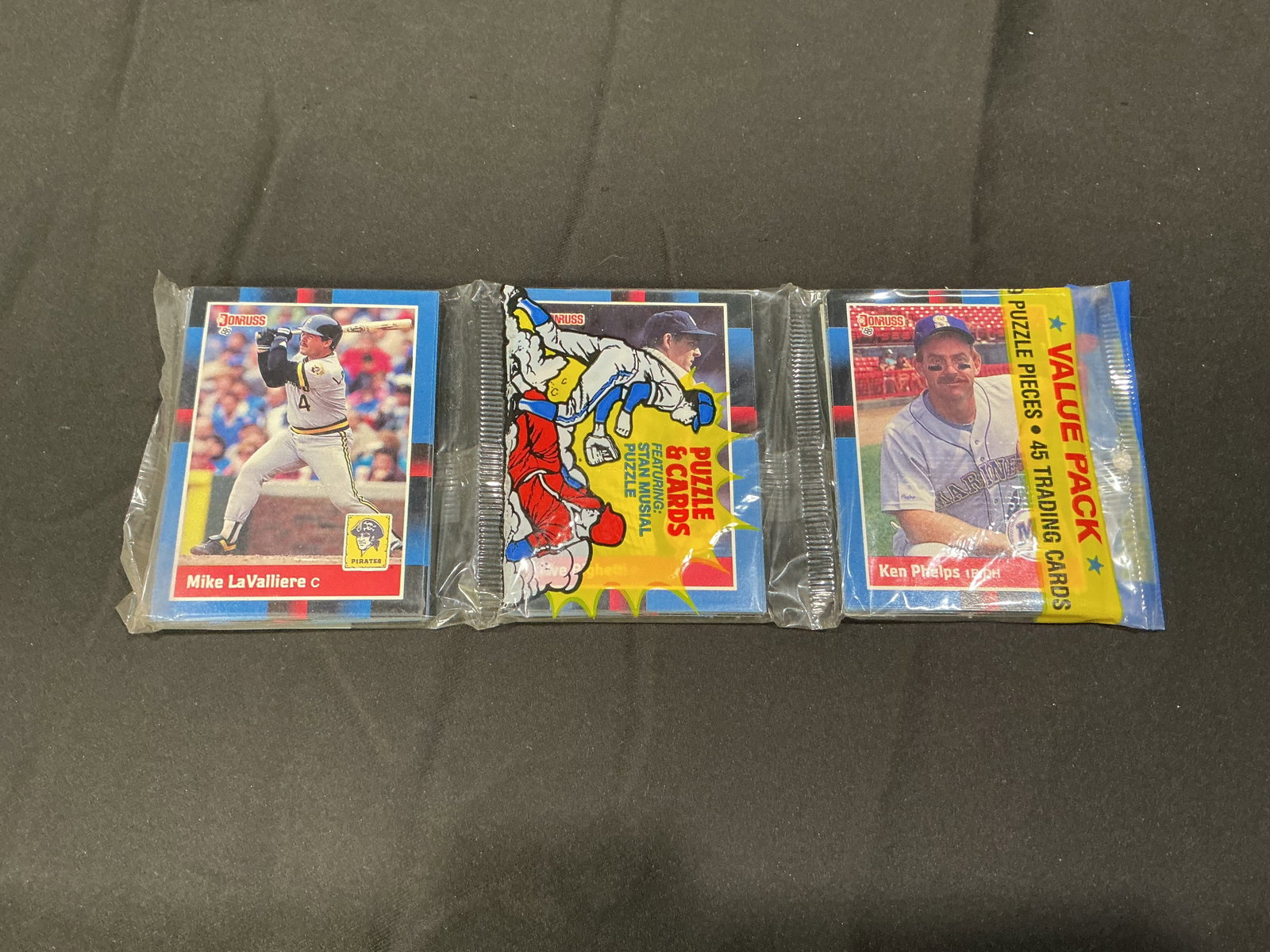 1988 Donruss Baseball Wax Pack Trio Ken Phelps Mike LaValliere: Three sealed 1988 Donruss baseball value packs featuring visible Ken Phelps and Mike LaValliere cards on packaging fronts. Includes puzzle and card promotional graphics typical of the era. Returning o