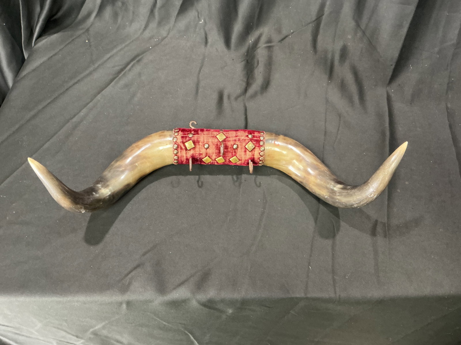 Longhorn Horn Wall Rack With Red Velvet Mount Hooks: Decorative longhorn horn wall rack featuring polished natural horns mounted to a red velvet covered center panel with metal hanging hooks. Western ranch and lodge style presentation suitable for coats