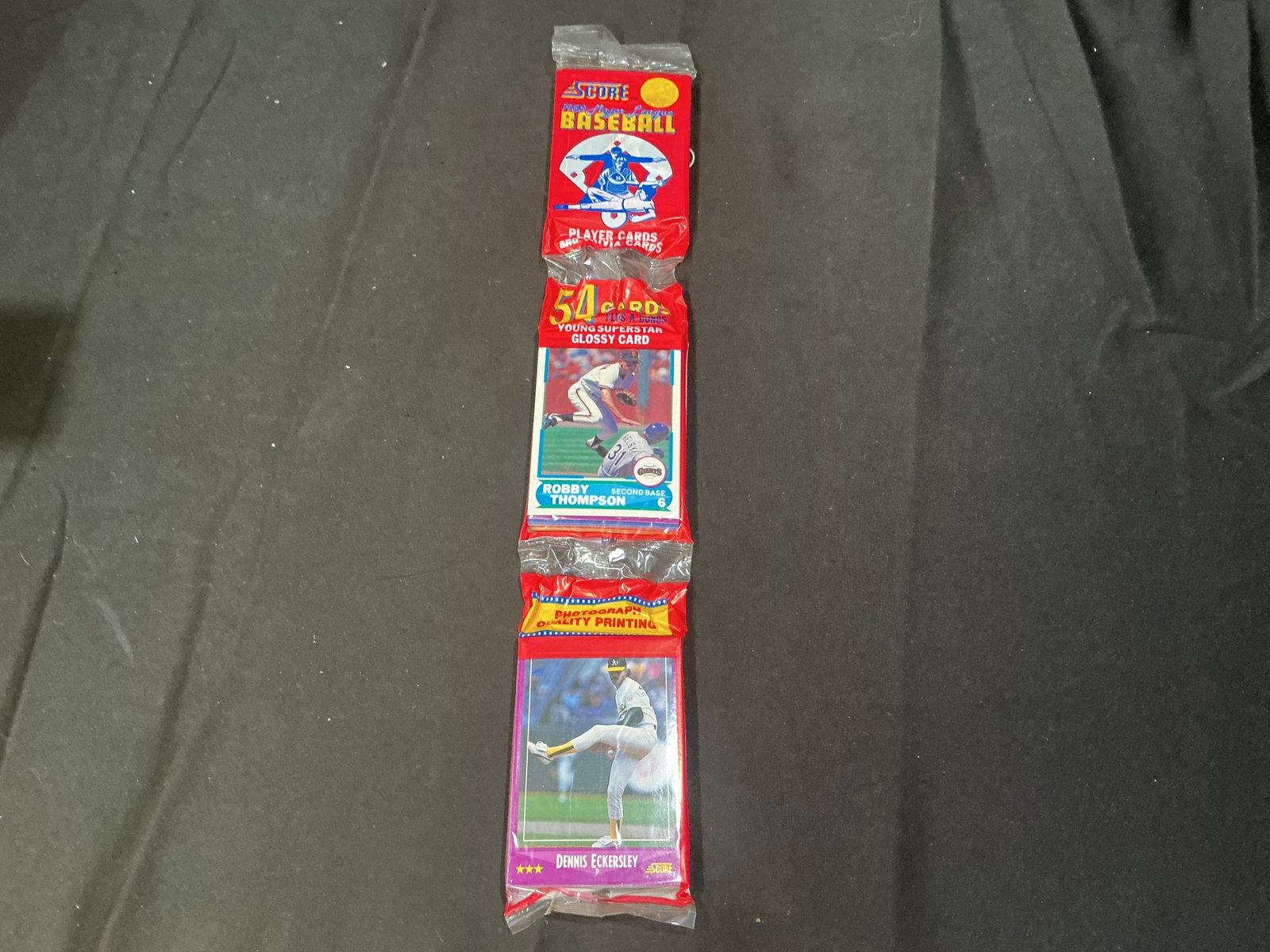 1990 Score Baseball Wax Pack Dennis Eckersley Bonus Card: Sealed 1990 Score Baseball wax pack containing 54 player and trivia cards plus bonus young superstar glossy card featuring Robby Thompson on wrapper and Dennis Eckersley glossy insert visible. Vintage