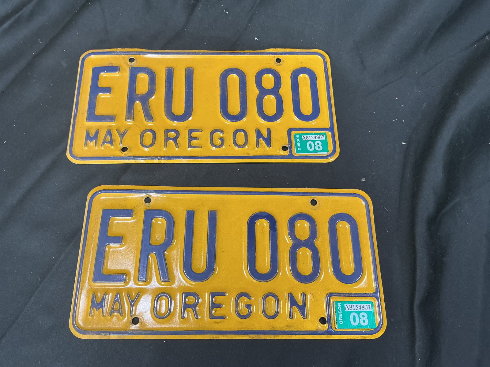 Matching Pair Oregon ERU 080 Vintage License Plates: Matching pair of vintage Oregon license plates numbered ERU 080 with yellow and blue color scheme and May Oregon registration tags. Strong garage decor, automobilia, and vintage transportation