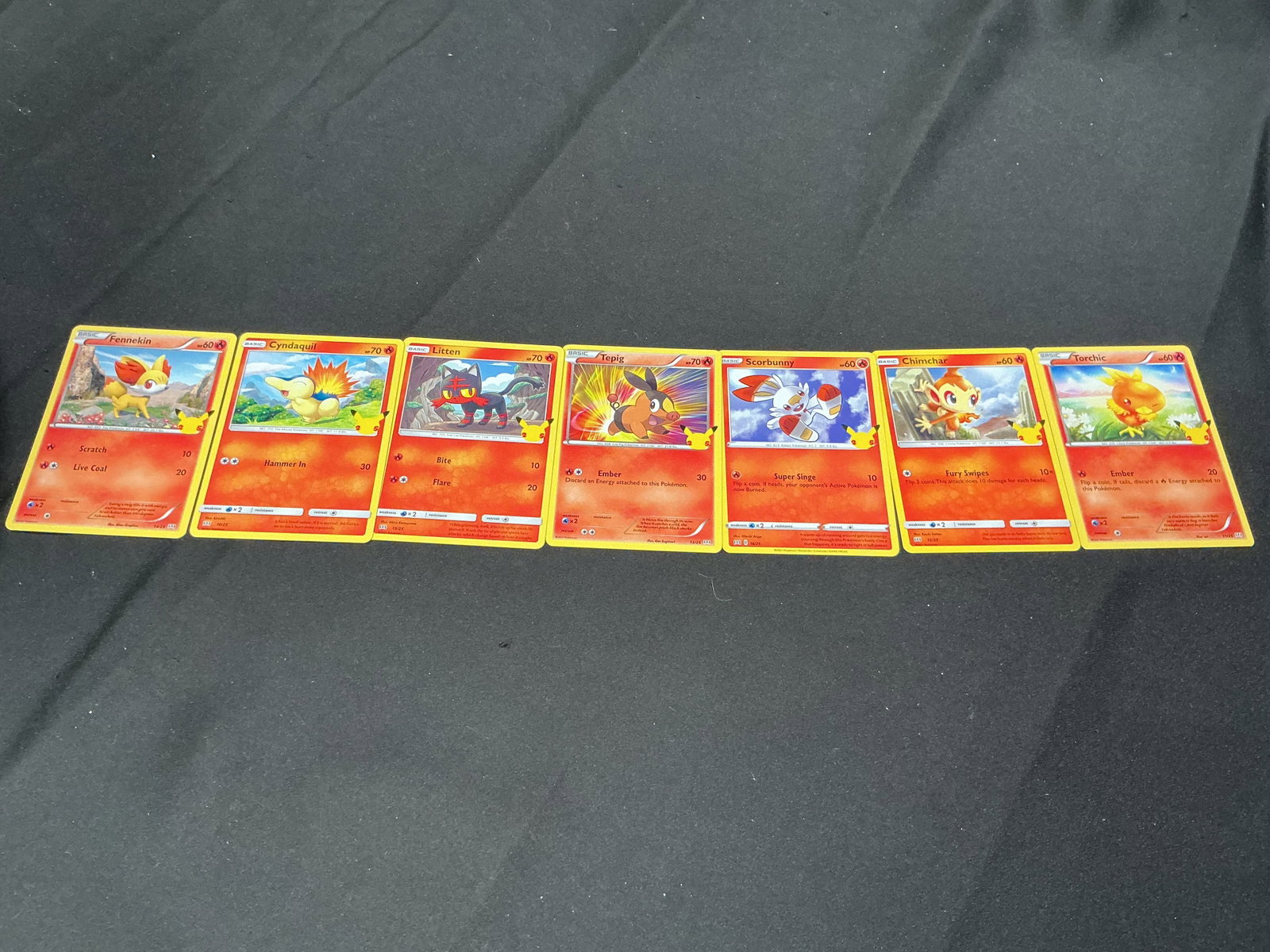 Pokemon 25th Anniversary Fire Starter Promo Card Lot Encore: Pokemon 25th Anniversary promotional card lot featuring Fennekin, Cyndaquil, Litten, Tepig, Scorbunny, Chimchar, and Torchic. Colorful starter Pokemon group with anniversary Pikachu stamp logos