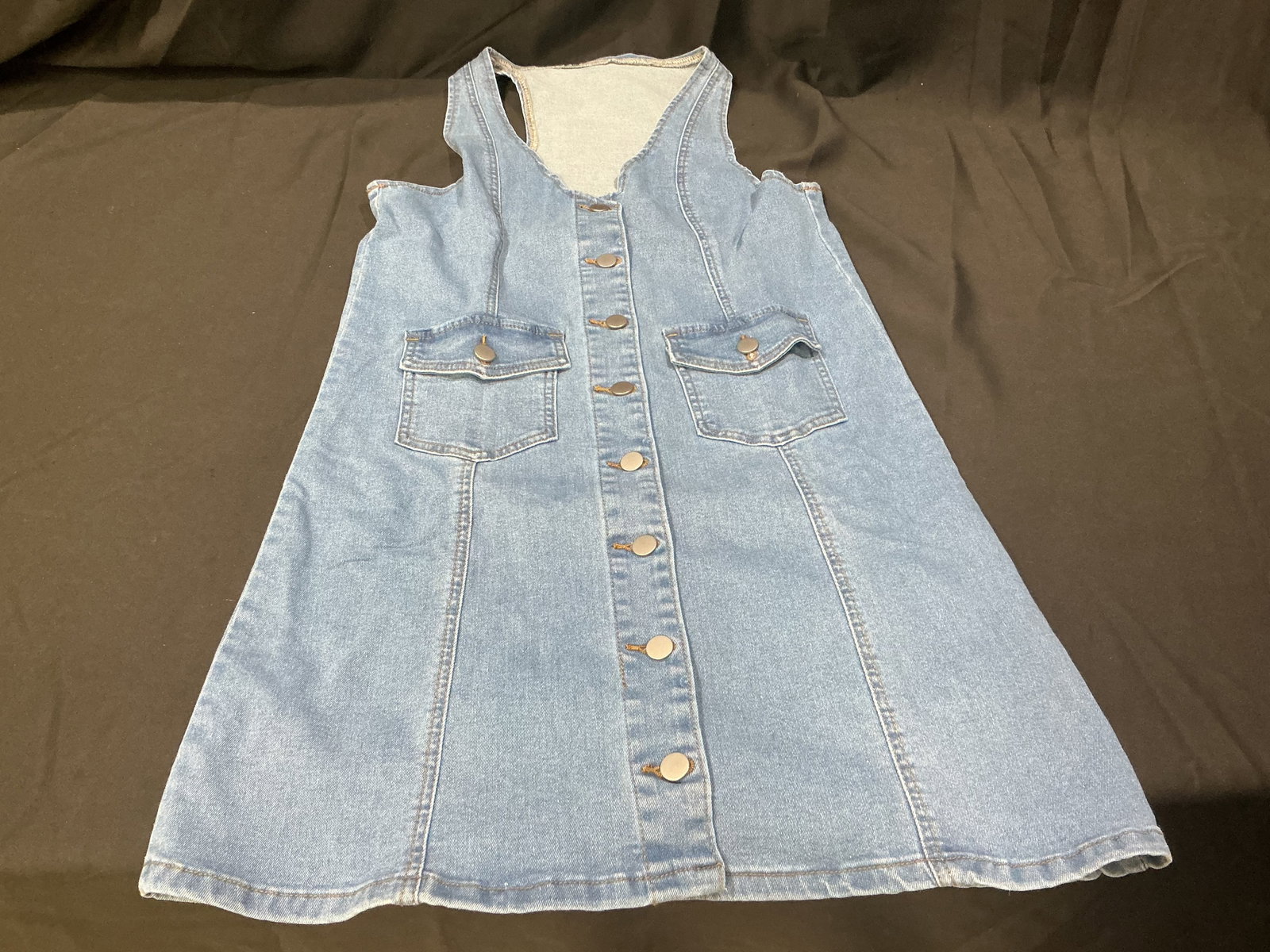 Light Blue Denim Style Sleeveless Button Front Dress: Light blue denim style sleeveless dress featuring button front closure and dual front pockets. Casual vintage-inspired fashion piece with flared cut and classic denim look. Still stored in original pa