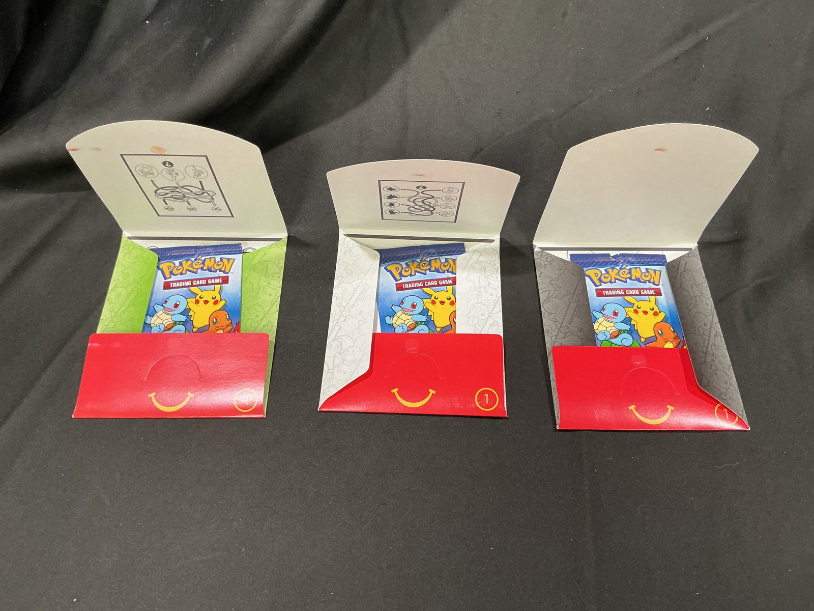 Pokemon McDonalds Promo Pack Trio Sealed Happy Meal Packs Returning Favorite Back Again: Group of three sealed Pokemon McDonalds Happy Meal promotional card packs with variant Pikachu packaging colors. Includes sealed promo packs featuring classic starter artwork presentation and