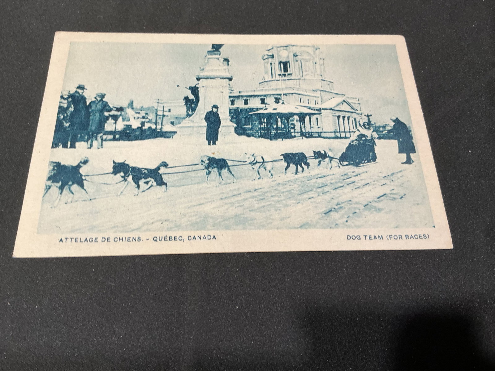 Vintage Quebec Dog Team Postcard: Offered once more, this vintage Quebec, Canada postcard depicts a dog team prepared for races in front of a prominent civic building. The unused example carries bilingual English and French captions