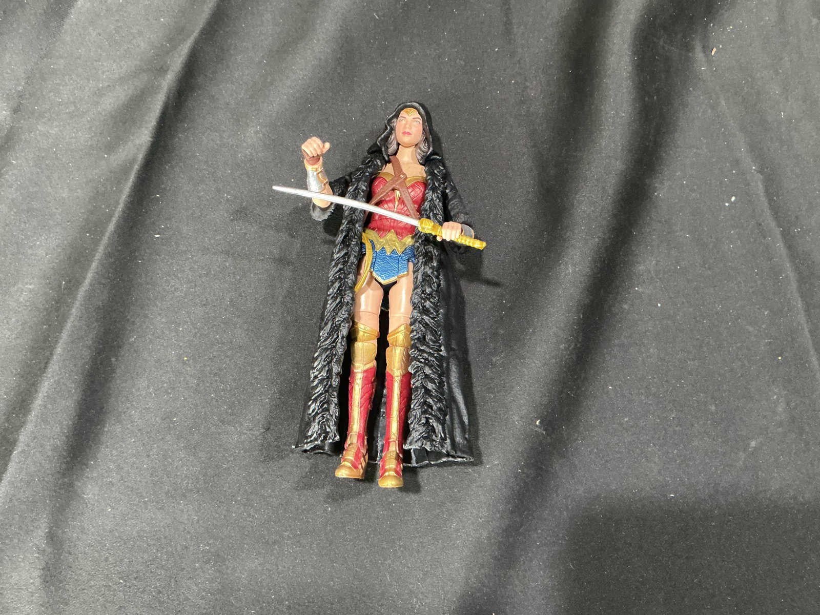DC Comics Wonder Woman Action Figure with Cloak and Sword: Returning to the auction lineup, this DC Comics Wonder Woman action figure wears a red and gold armored bodice, blue skirt, gold tiara, and red and gold boots. Includes a long black hooded cloak and