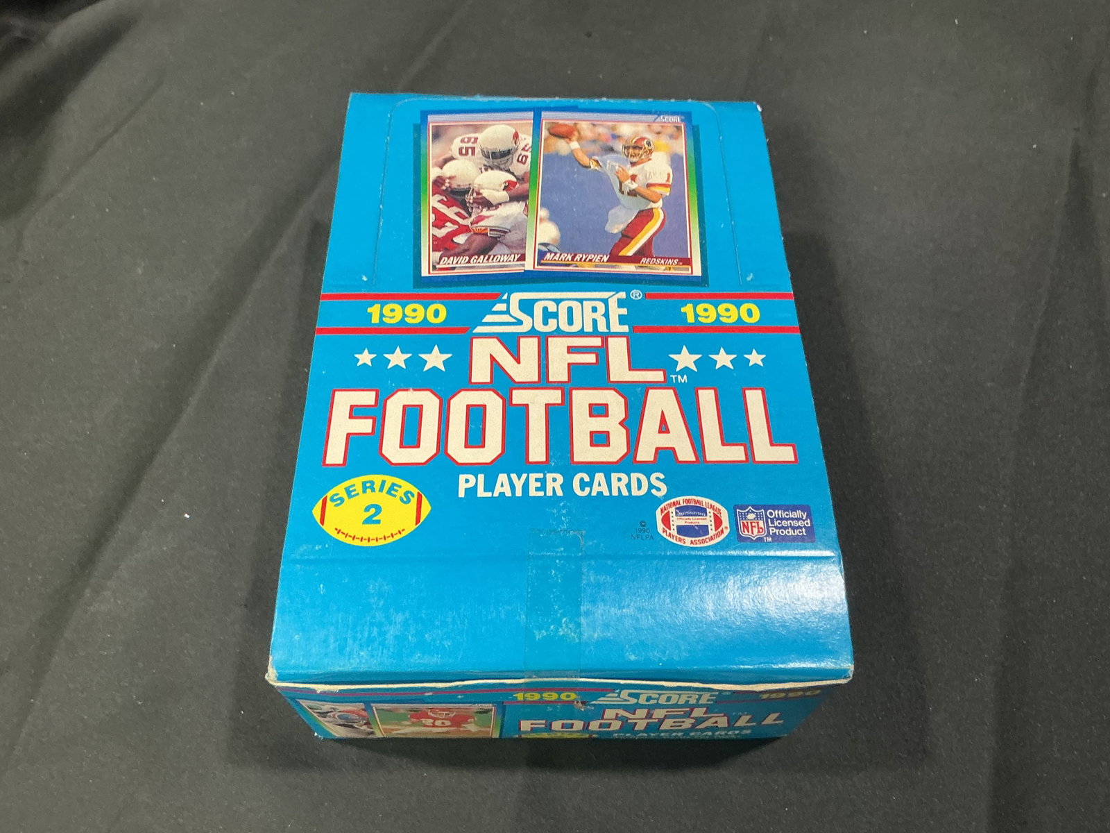 1990 Score NFL Series 2 Wax Box: Making another appearance, this 1990 Score NFL Football Series 2 factory box contains unopened packs of vintage football cards. The classic wax-box format offers collectors a chance at stars and Hall