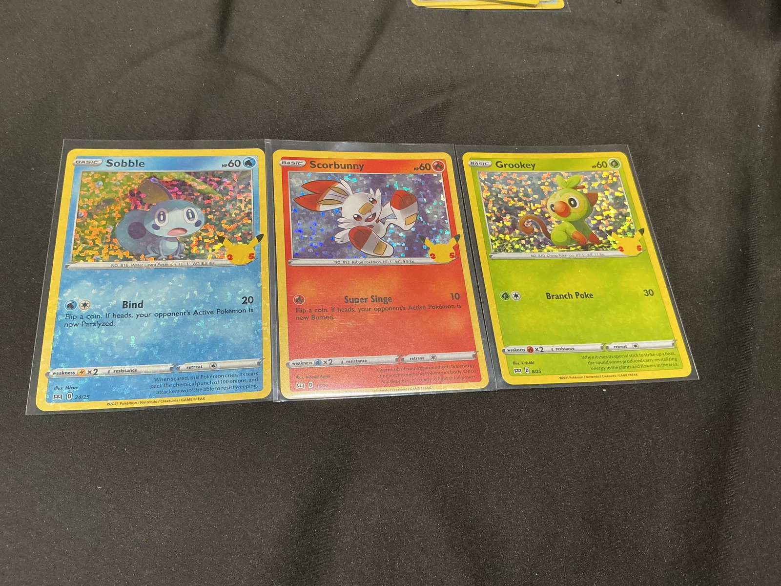Pokemon 25th Anniversary Galar Starter Holo Trio: A colorful Pokemon 25th Anniversary holo card trio featuring the Galar starters Sobble #24/25, Scorbunny #16/25, and Grookey #8/25. Each card features the Pikachu 25th Anniversary stamp and a