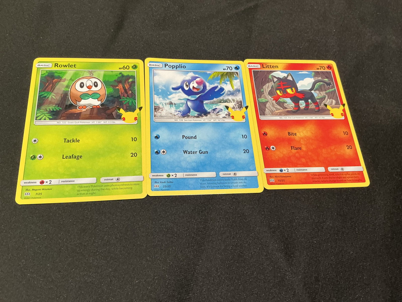 Pokemon 25th Anniversary Alola Starter Trio: Pokemon 25th Anniversary three-card starter grouping featuring Rowlet #7/25, Popplio #23/25, and Litten #15/25. Each card carries the Pikachu 25th anniversary stamp and together the trio represents