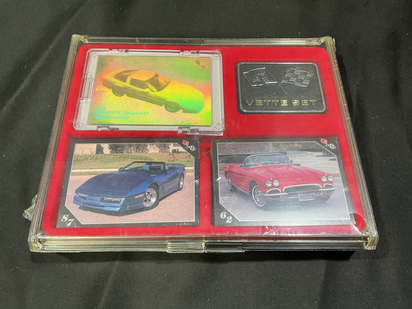 Corvette Vette Set Collector Card Display: Vintage Corvette Vette Set collector display featuring Corvette-themed trading cards and an emblem-style Vette Set plaque arranged in a red presentation case. Visible cards include a holographic 1988 