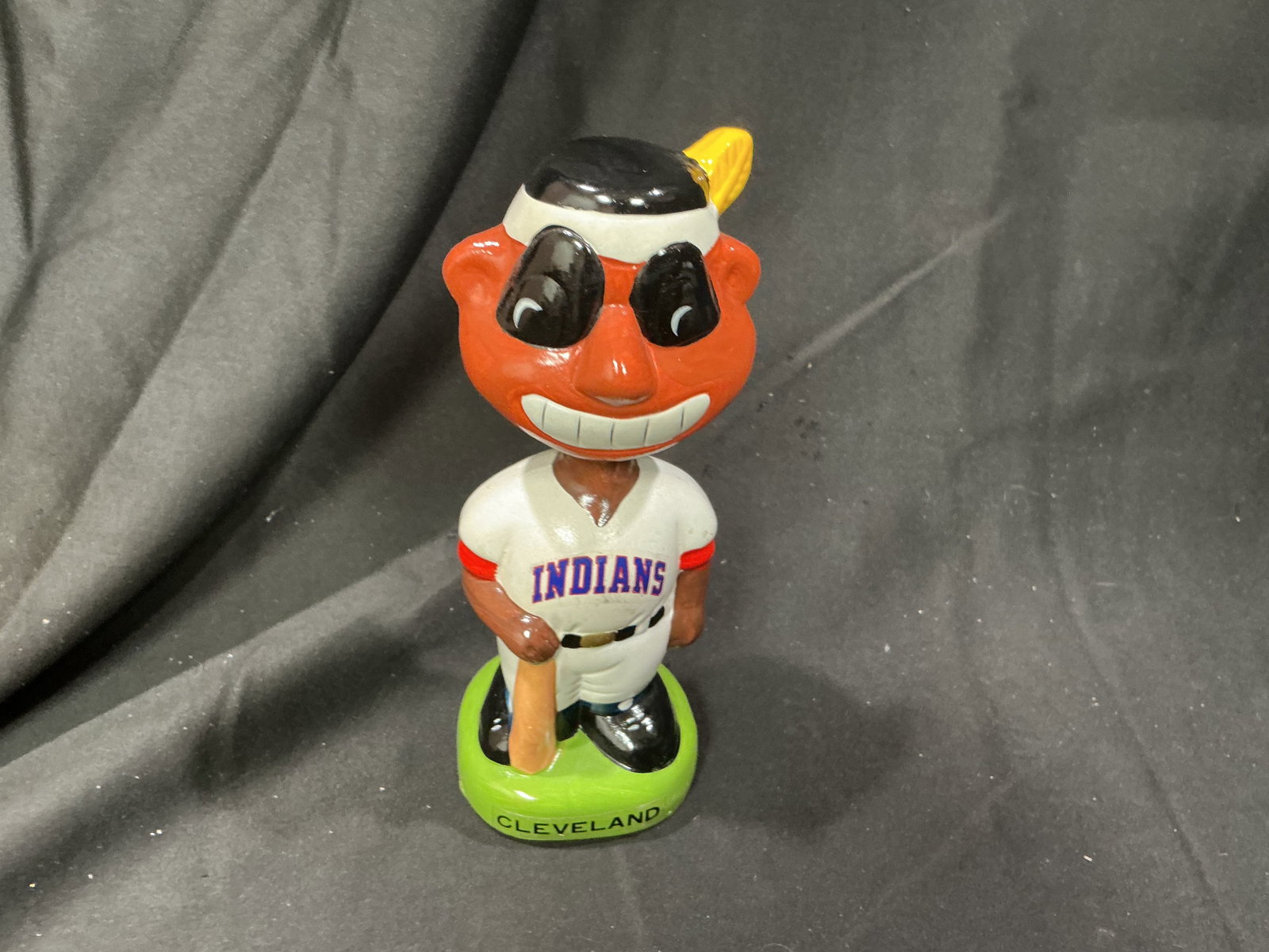 Cleveland Indians Chief Wahoo Baseball Bobblehead: A colorful Cleveland Indians baseball bobblehead featuring the team's former Chief Wahoo mascot in a white Indians uniform, black war-paint-style markings around the eyes, a feathered headband, and ho
