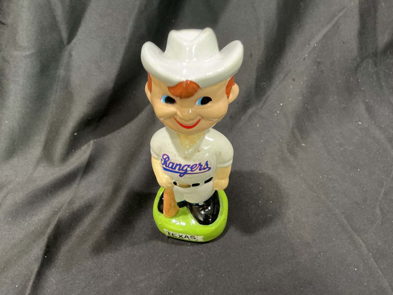 Vintage Texas Rangers Cowboy Green Base Nodder: Offered for the first time in our auction, this vintage Texas Rangers baseball nodder features a smiling cowboy character in a Rangers uniform and oversized white cowboy hat, standing on a bright