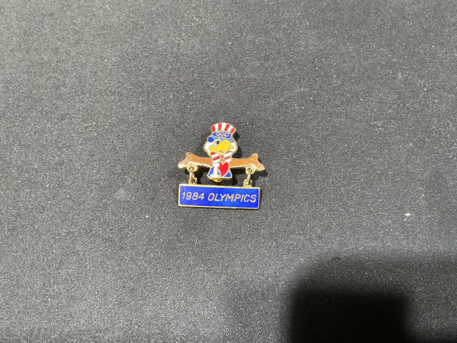 1984 Los Angeles Olympics Sam the Eagle Dangle Pin: This colorful 1984 Olympics pin features Sam the Olympic Eagle, the official mascot of the Los Angeles Games, dressed in patriotic red, white and blue with the Olympic rings on his hat. A suspended
