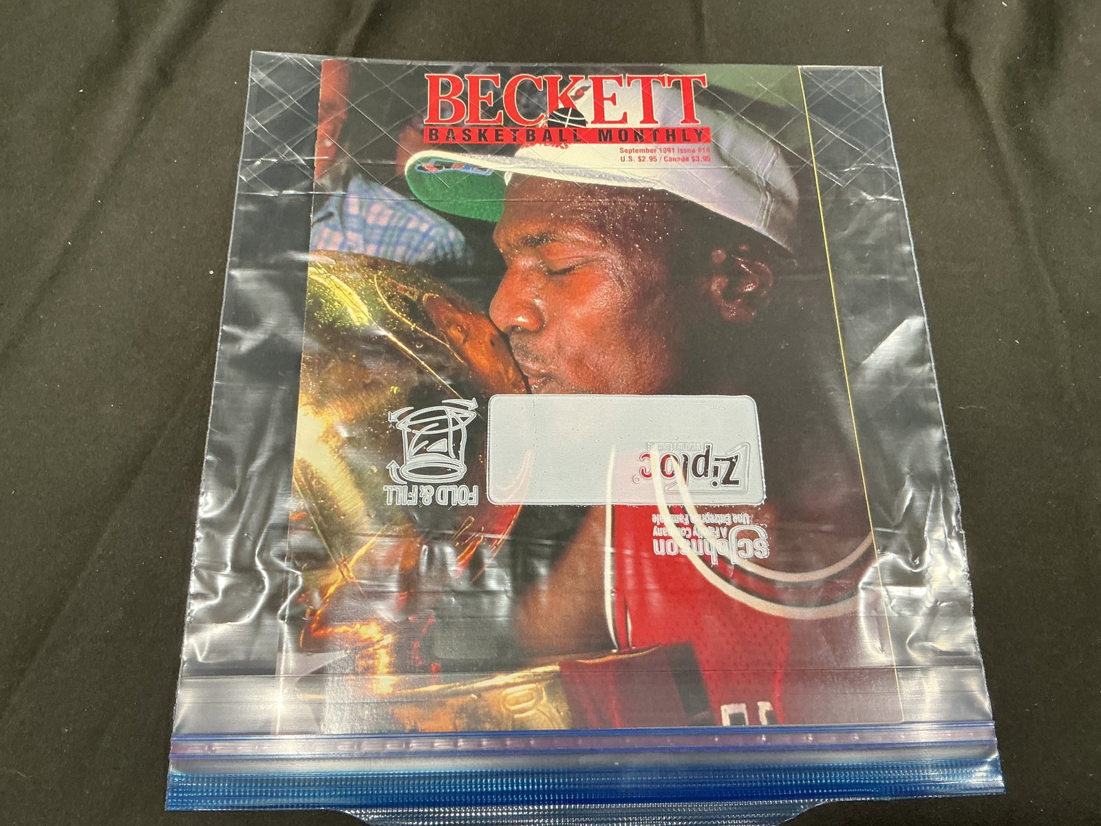 1991 Beckett Basketball Michael Jordan & Larry Johnson Magazine: A September 1991 issue of Beckett Basketball Monthly features Michael Jordan on the front cover kissing the Chicago Bulls' NBA championship trophy following the franchise's first title. The reverse