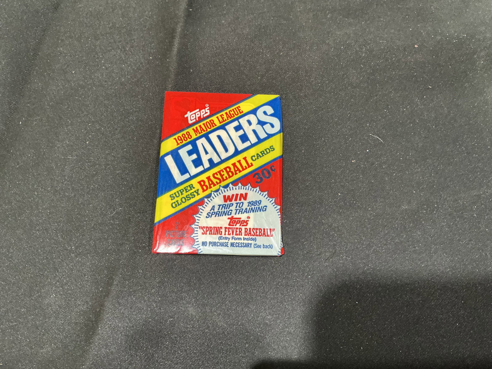 1988 Topps Major League Leaders Unopened Baseball Pack: Still sealed in its original colorful wrapper, this 1988 Topps Major League Leaders pack contains seven glossy baseball cards from the compact leader set. The period wrapper advertises the Topps Sprin