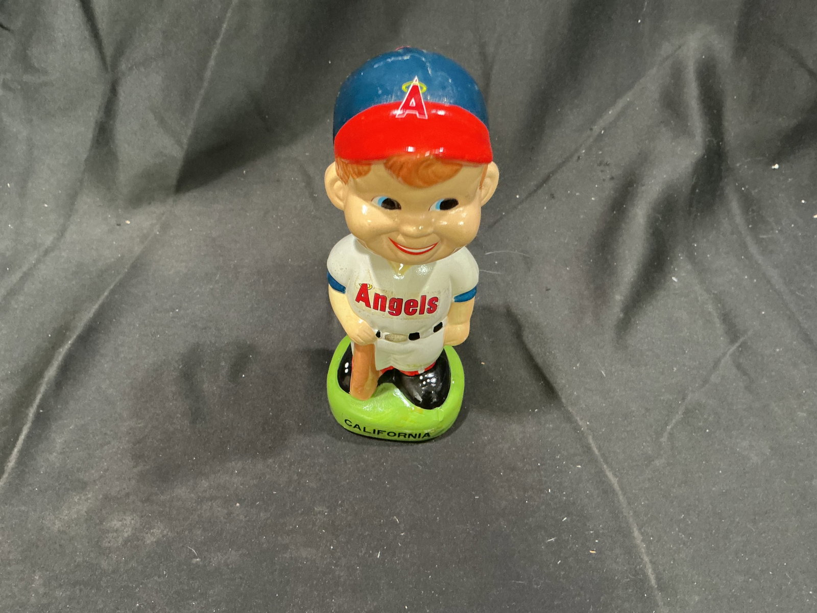 Vintage California Angels Baseball Player Bobblehead: A vintage-style California Angels baseball player bobblehead features a smiling batter in a white Angels uniform, red-and-blue cap, and black cleats, standing on a bright green base marked